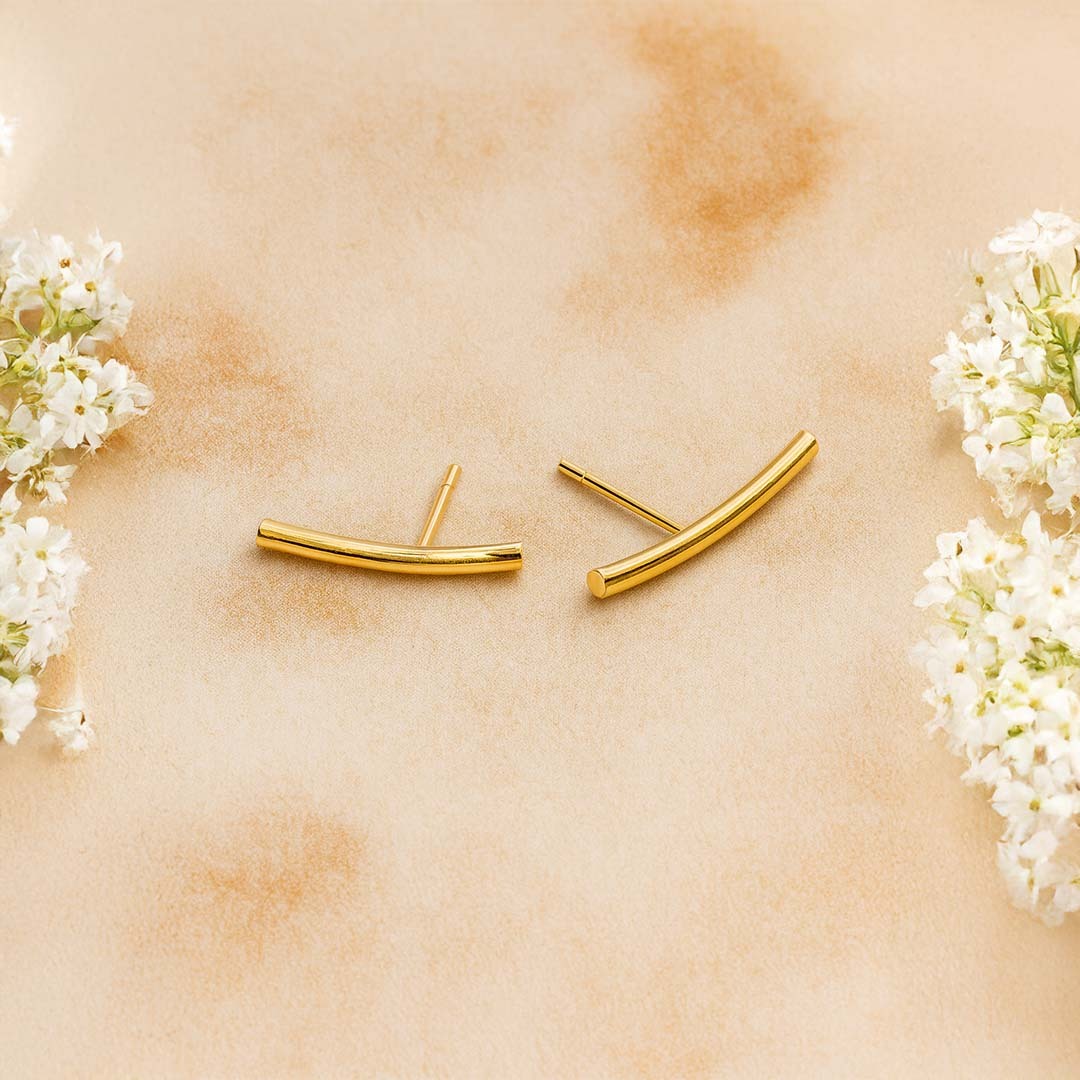 Gold earrings on a beige surface with white flowers