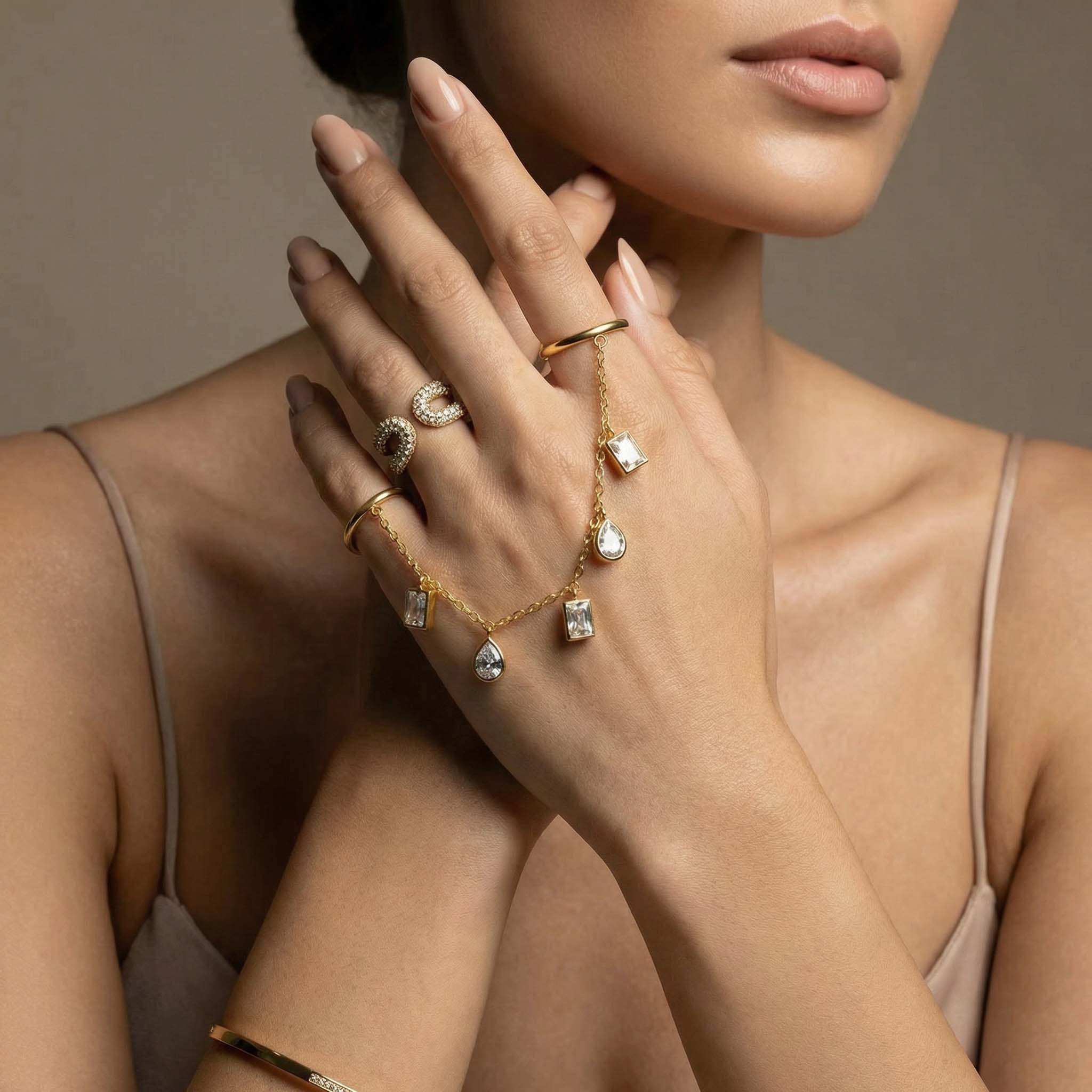 Close-up of a woman's hand wearing multiple gold rings with gemstones on a neutral background