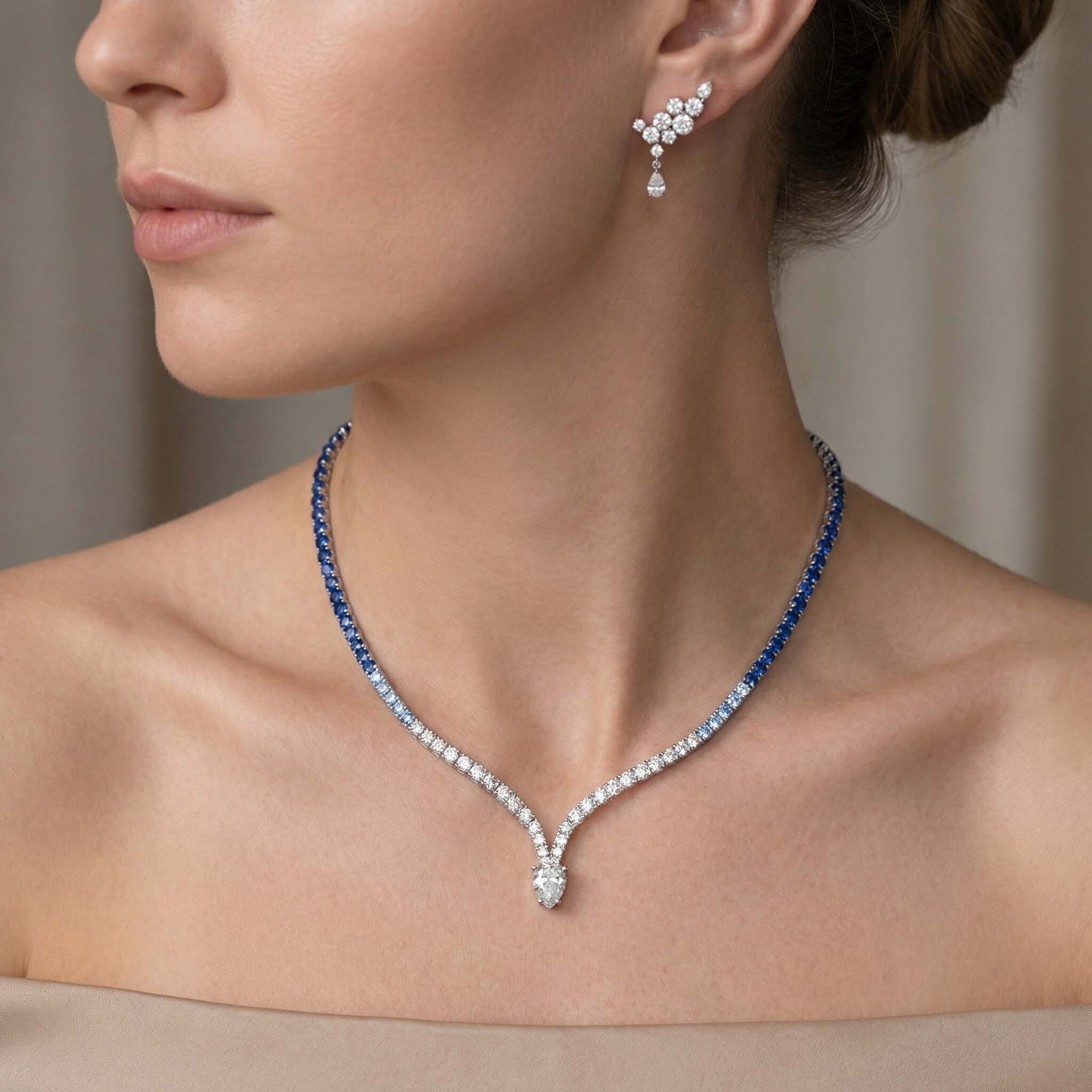 Close-up of a woman wearing a diamond necklace and earrings with a neutral background