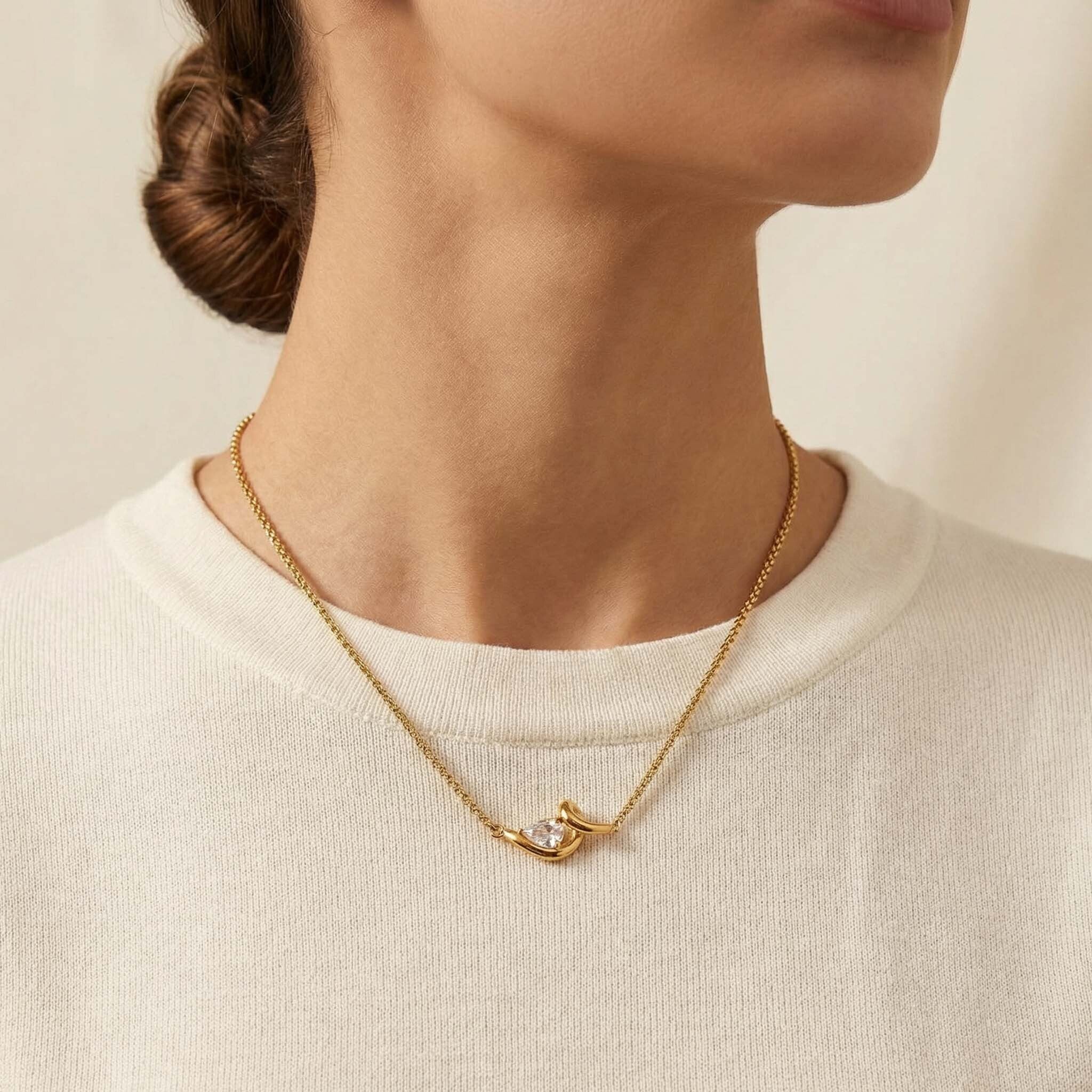Gold necklace with a diamond pendant worn by a person against a neutral background