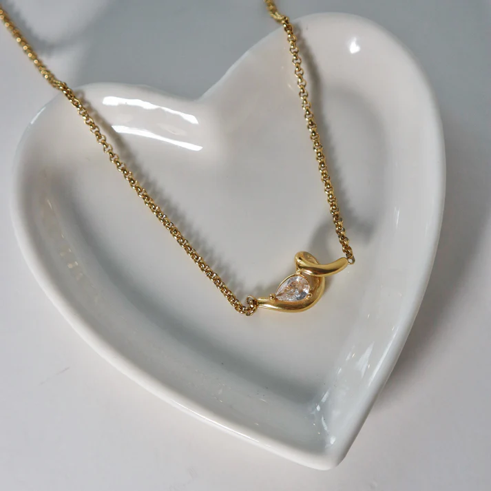 Gold necklace with a heart-shaped pendant on a white heart-shaped dish.