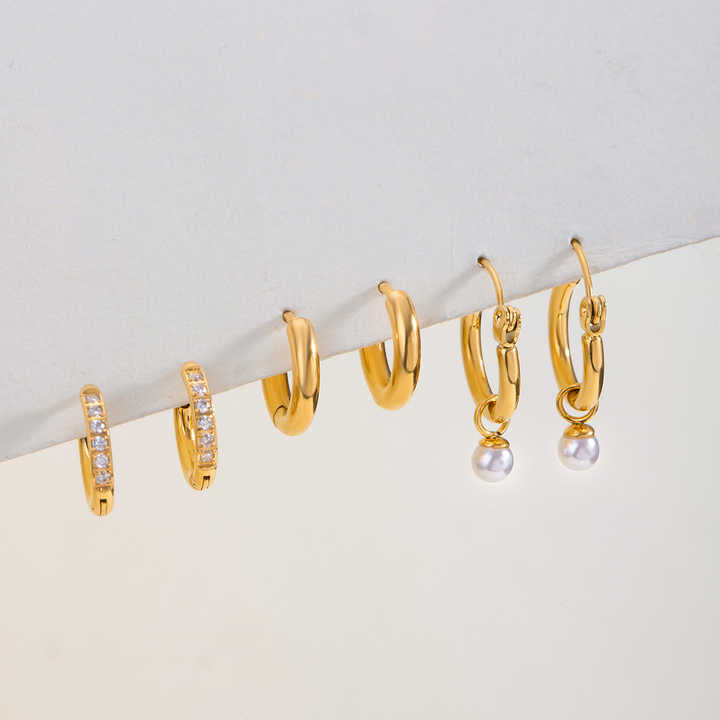 Set of gold hoop earrings for women with pearl on a light gray background