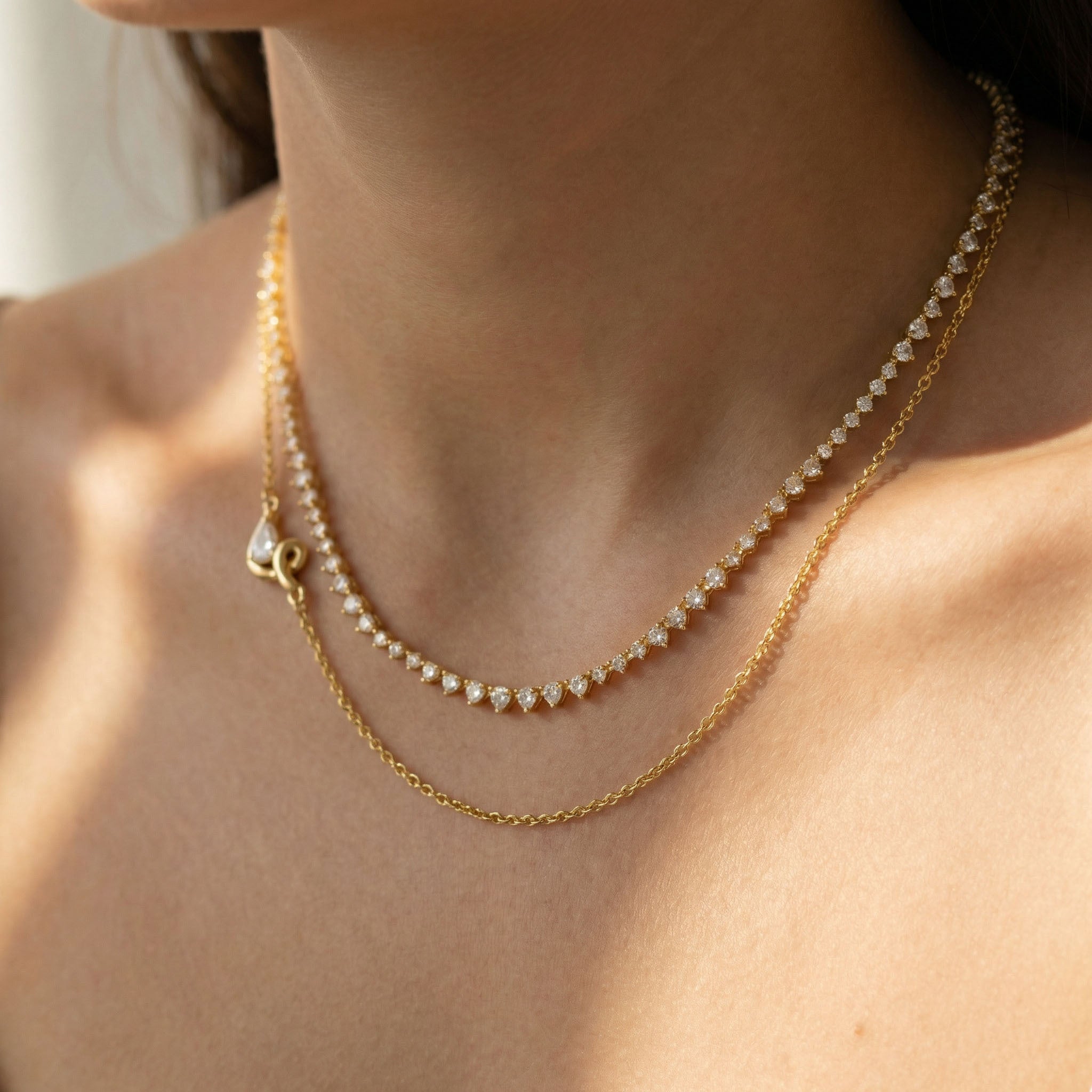 Close-up of a person wearing two gold necklaces with a blurred background