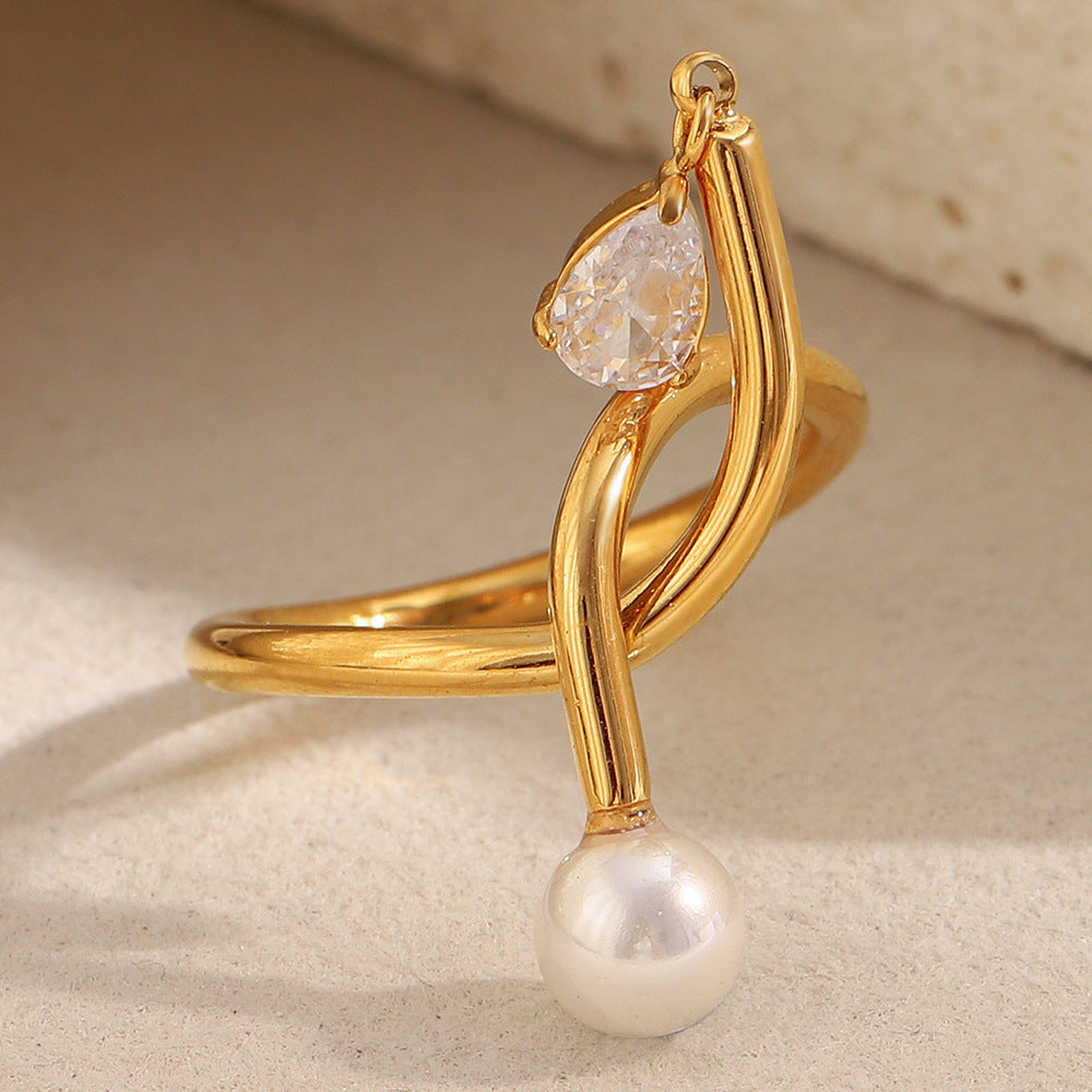 Gold ring with a teardrop-shaped gemstone and pearl on a beige background