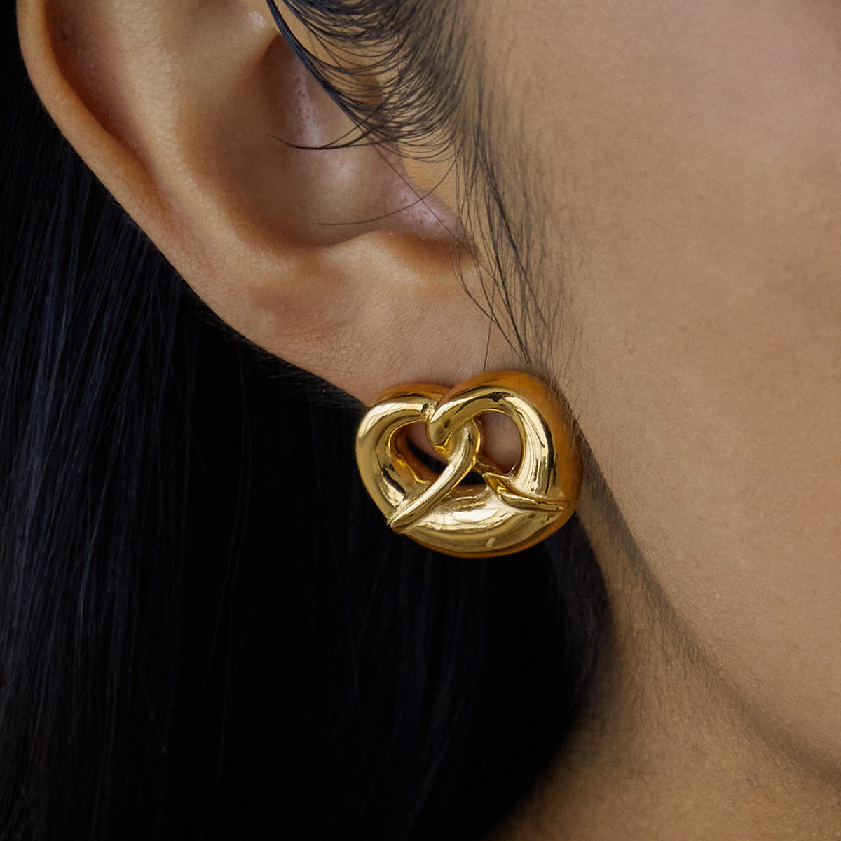 Gold heart-shaped earrings for women worn by a person with black hair.