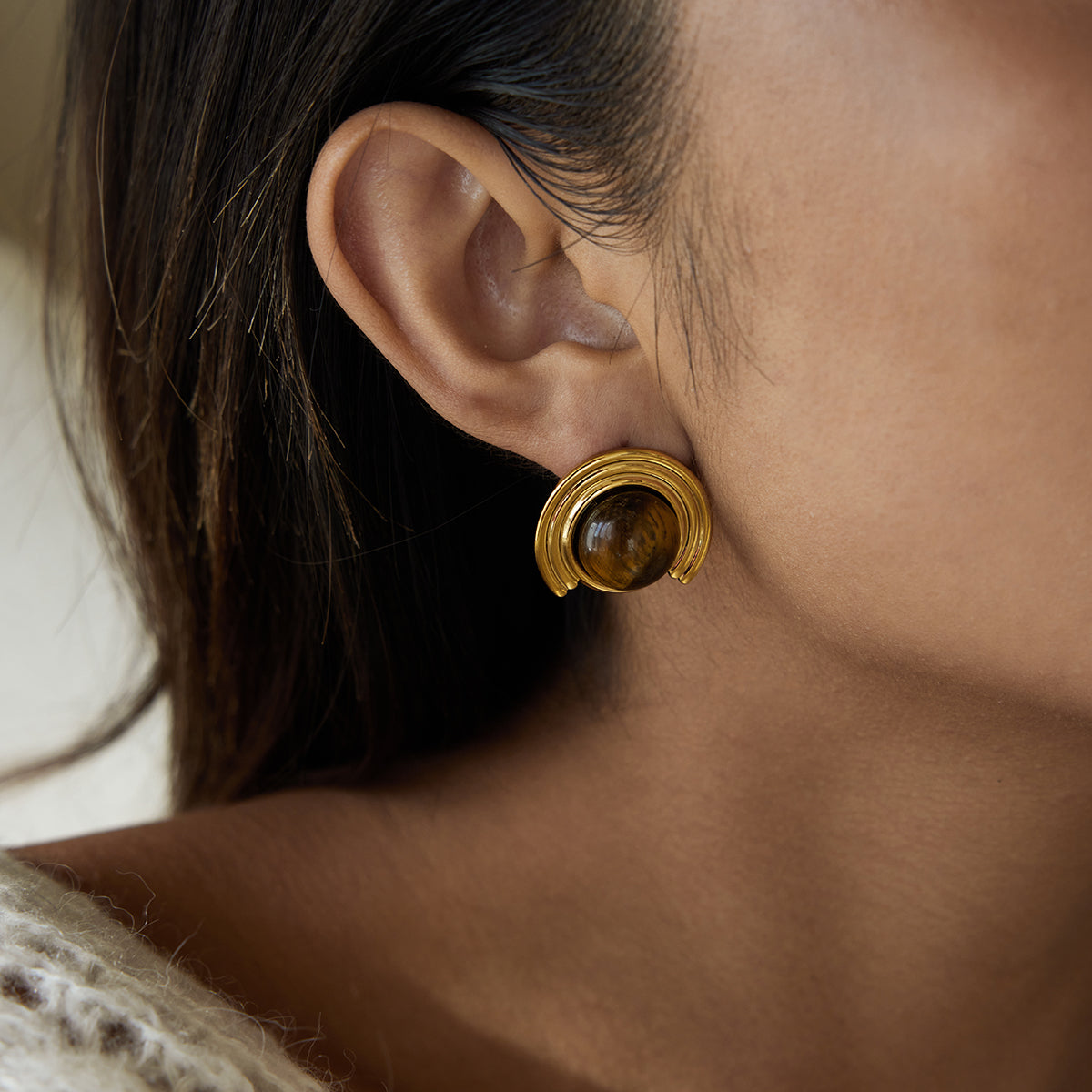 Close-up of a person wearing a gold earring for women with a brown gemstone.