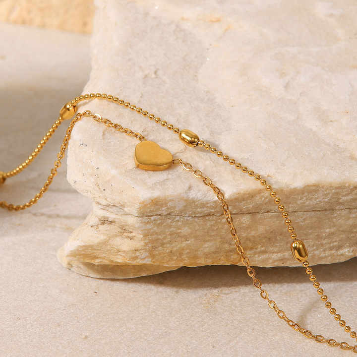Gold heart-shaped pendant anklet on a stone surface