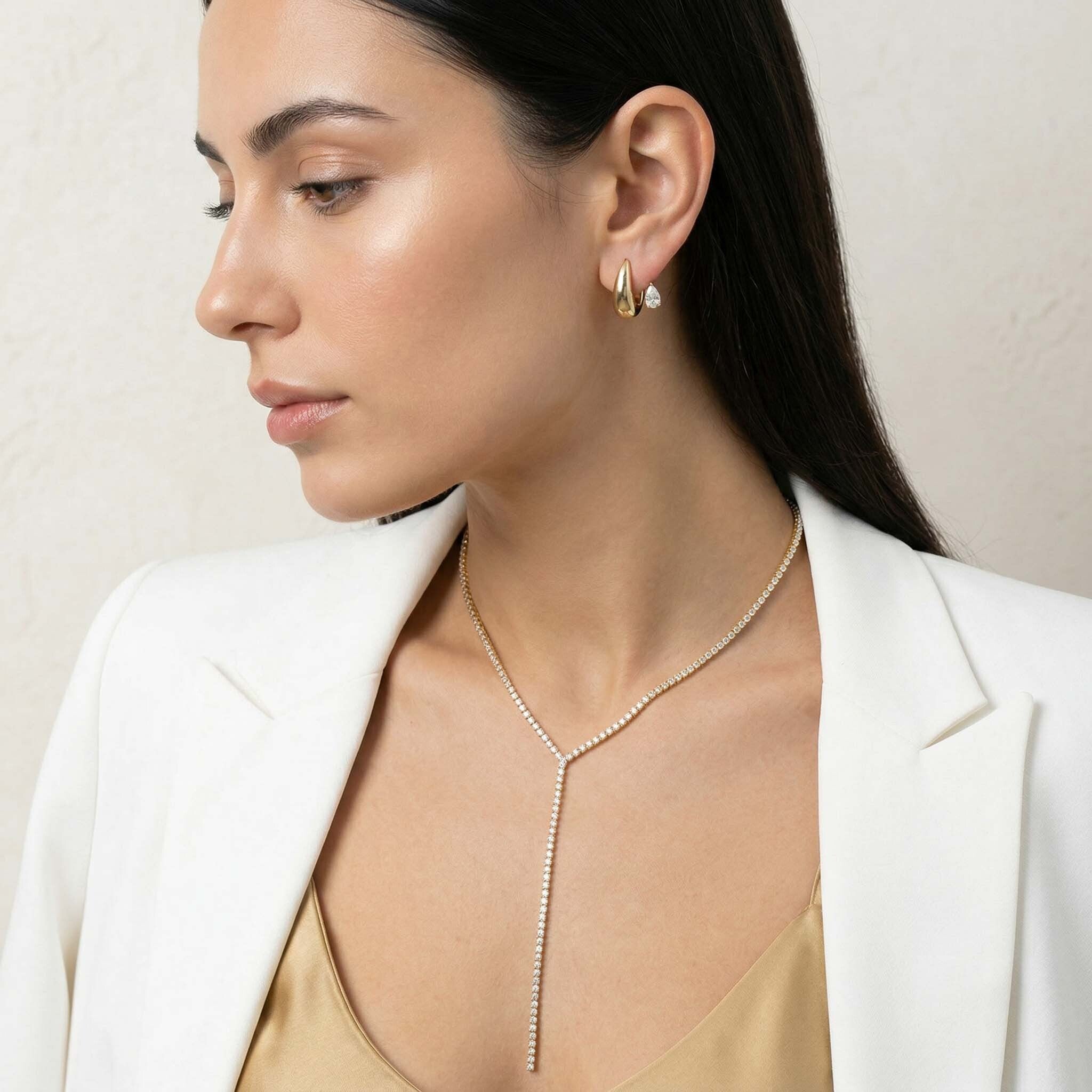 Woman wearing a delicate necklace and earrings against a neutral background