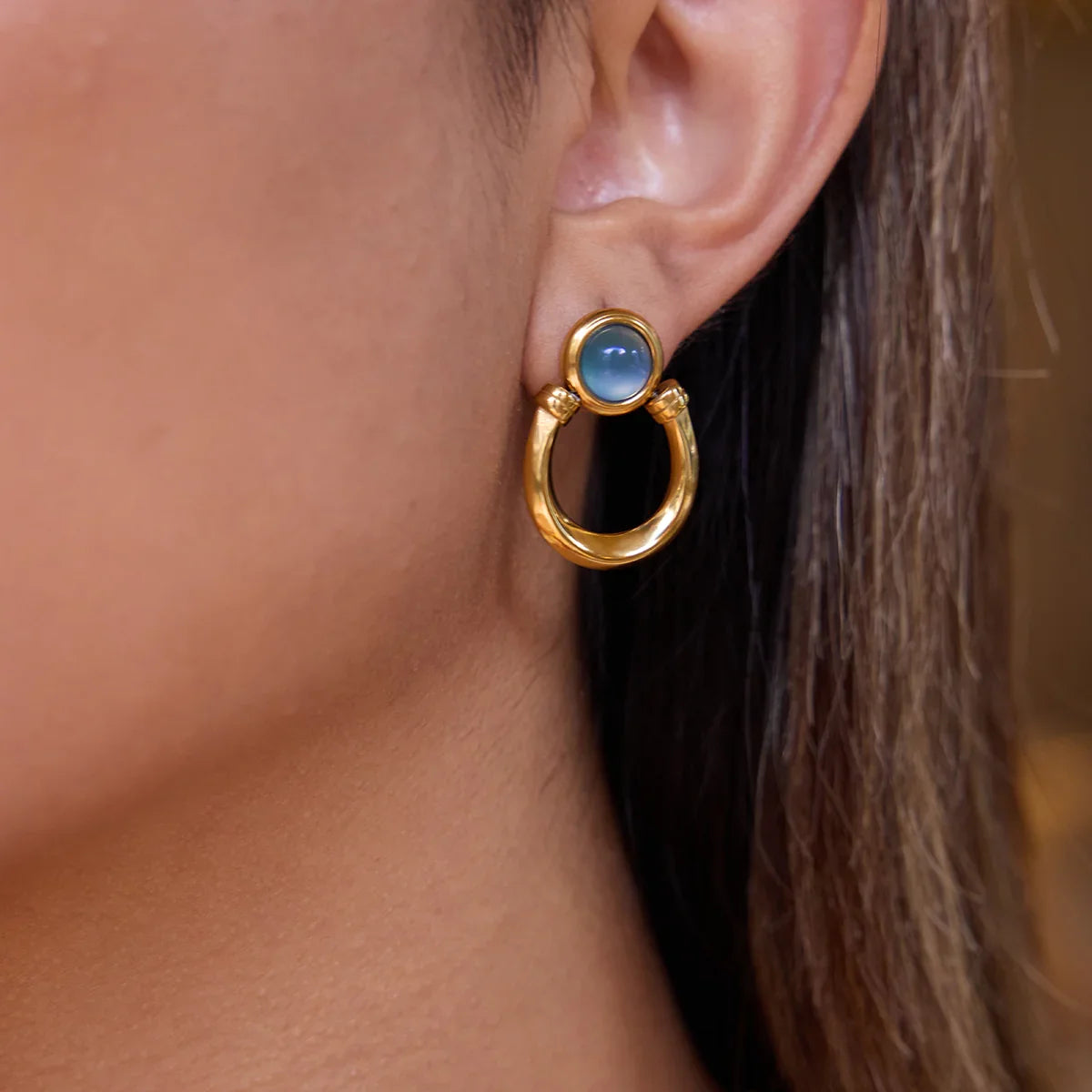 Gold earrings for women with a blue gemstone worn by a person
