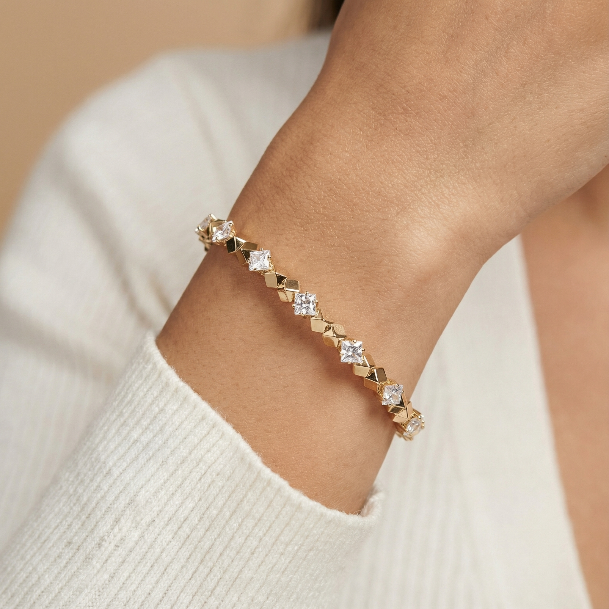 gold bracelet with diamonds on a wrist against a beige background