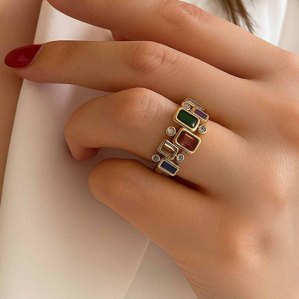 Gold ring with colored stones on a hand against a white background