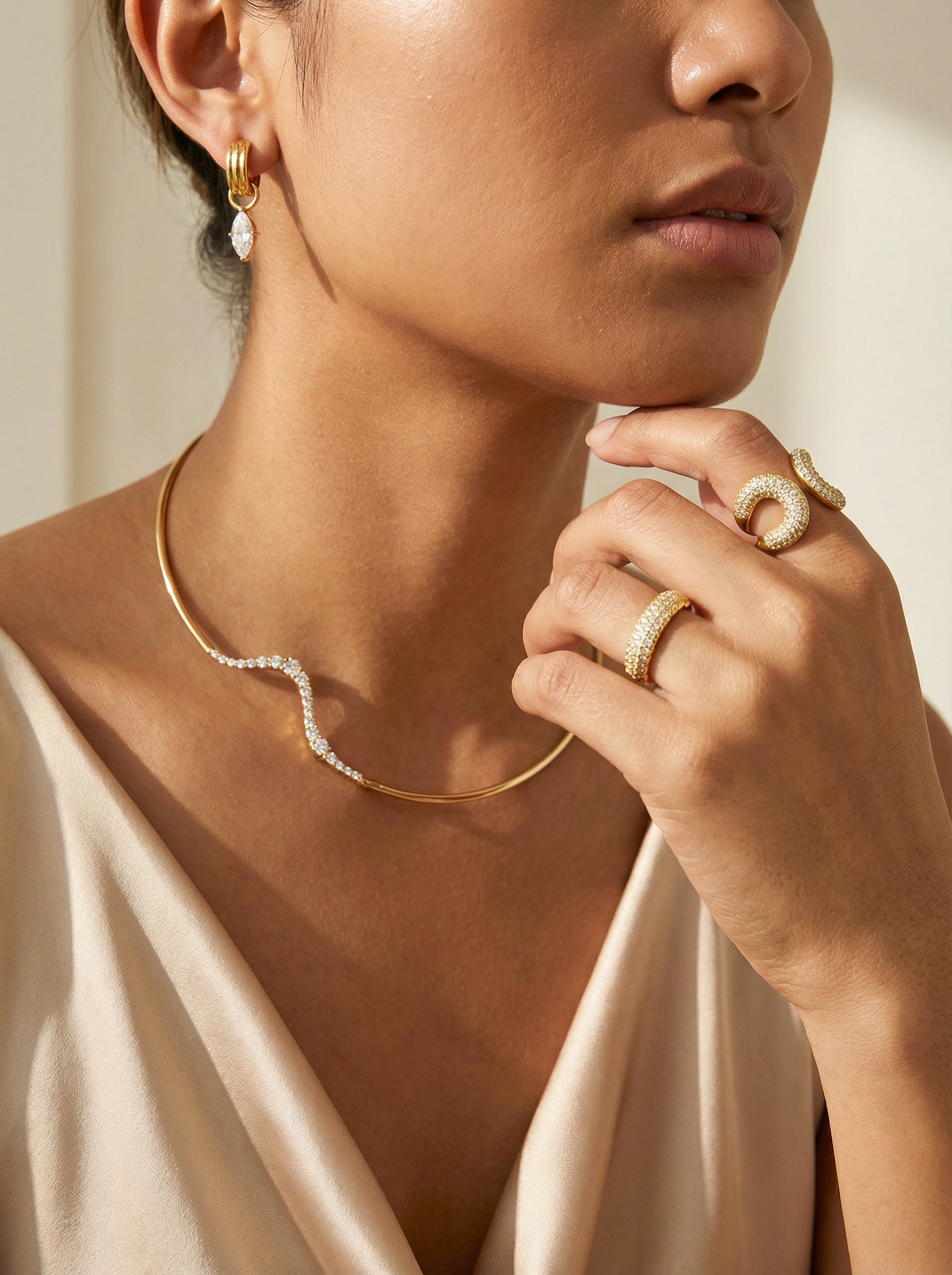 Close-up of a person wearing gold jewelry including a necklace, earrings, and rings.