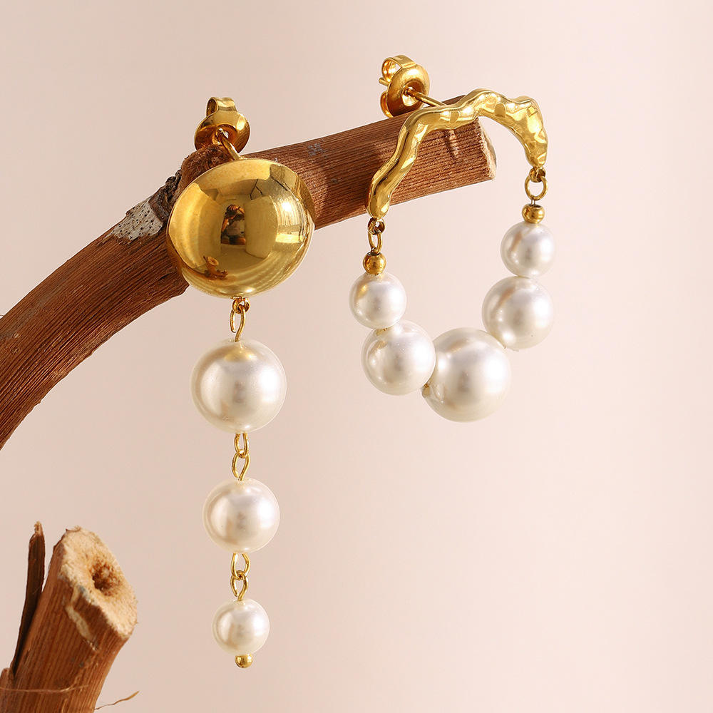 Gold and pearl earrings for women on a wooden branch against a beige background