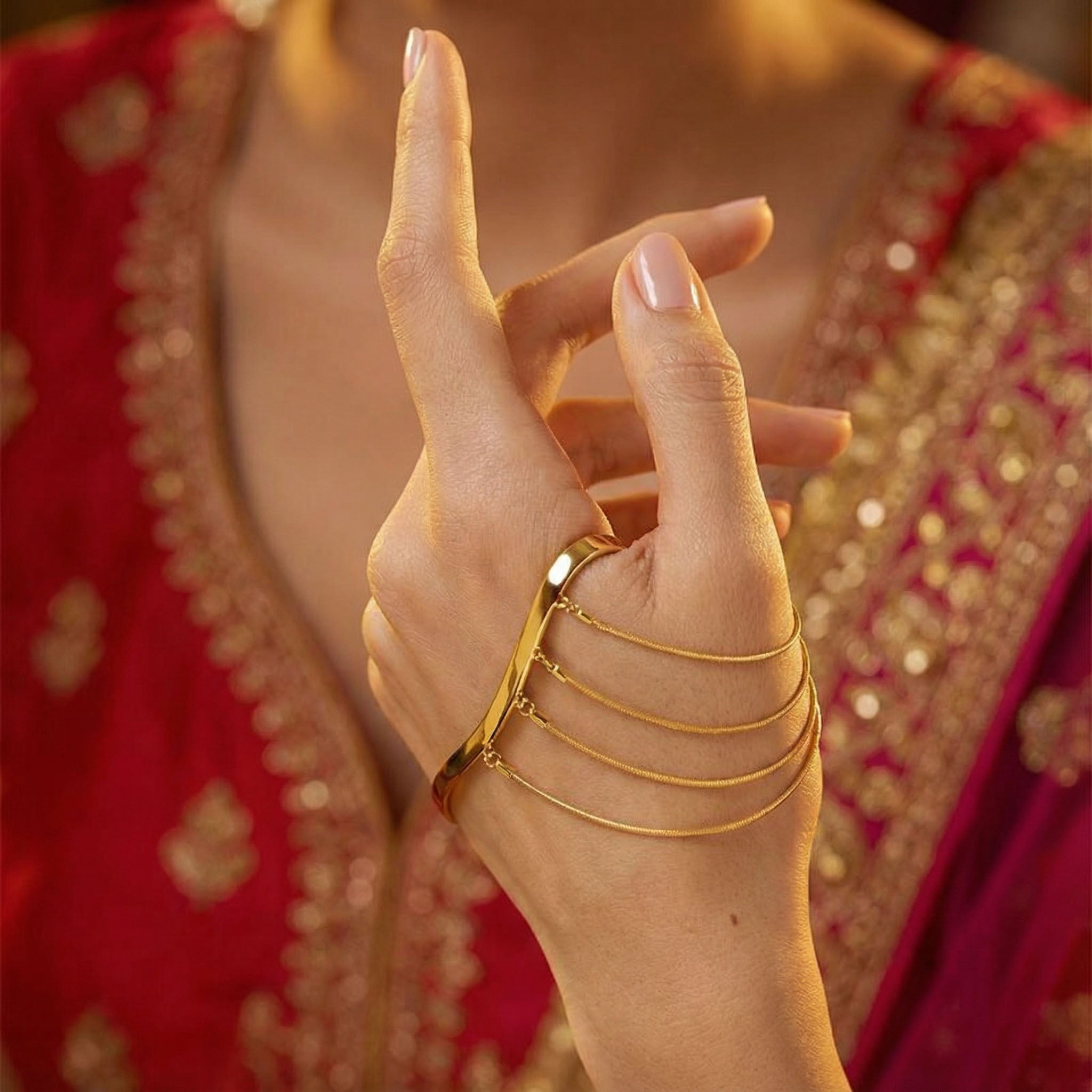 Hand wearing gold bracelets with a red and gold traditional outfit in the background