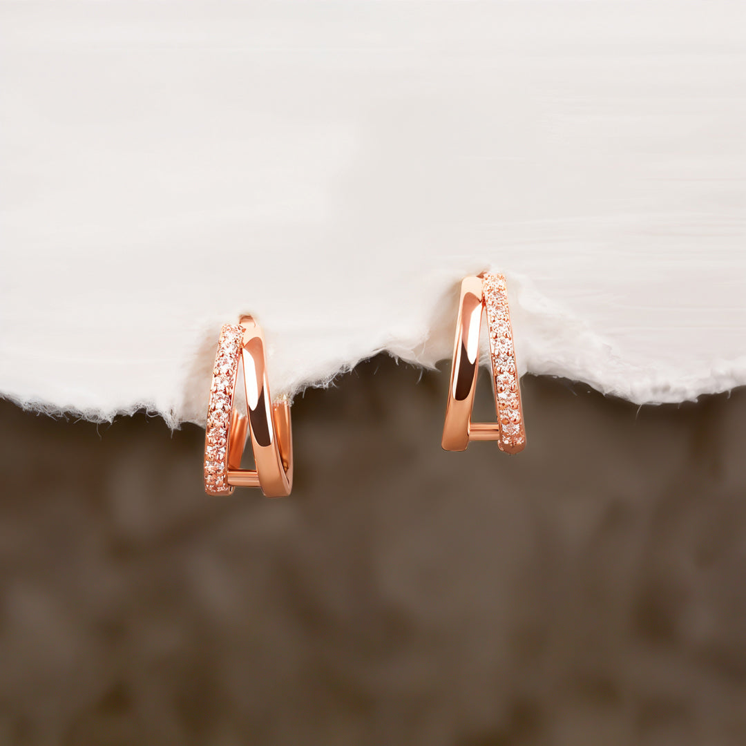 Rose gold hoop earrings with small diamonds on a textured surface