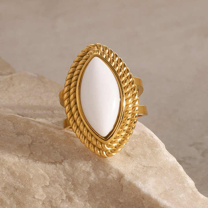Gold ring with a white stone on a beige rock