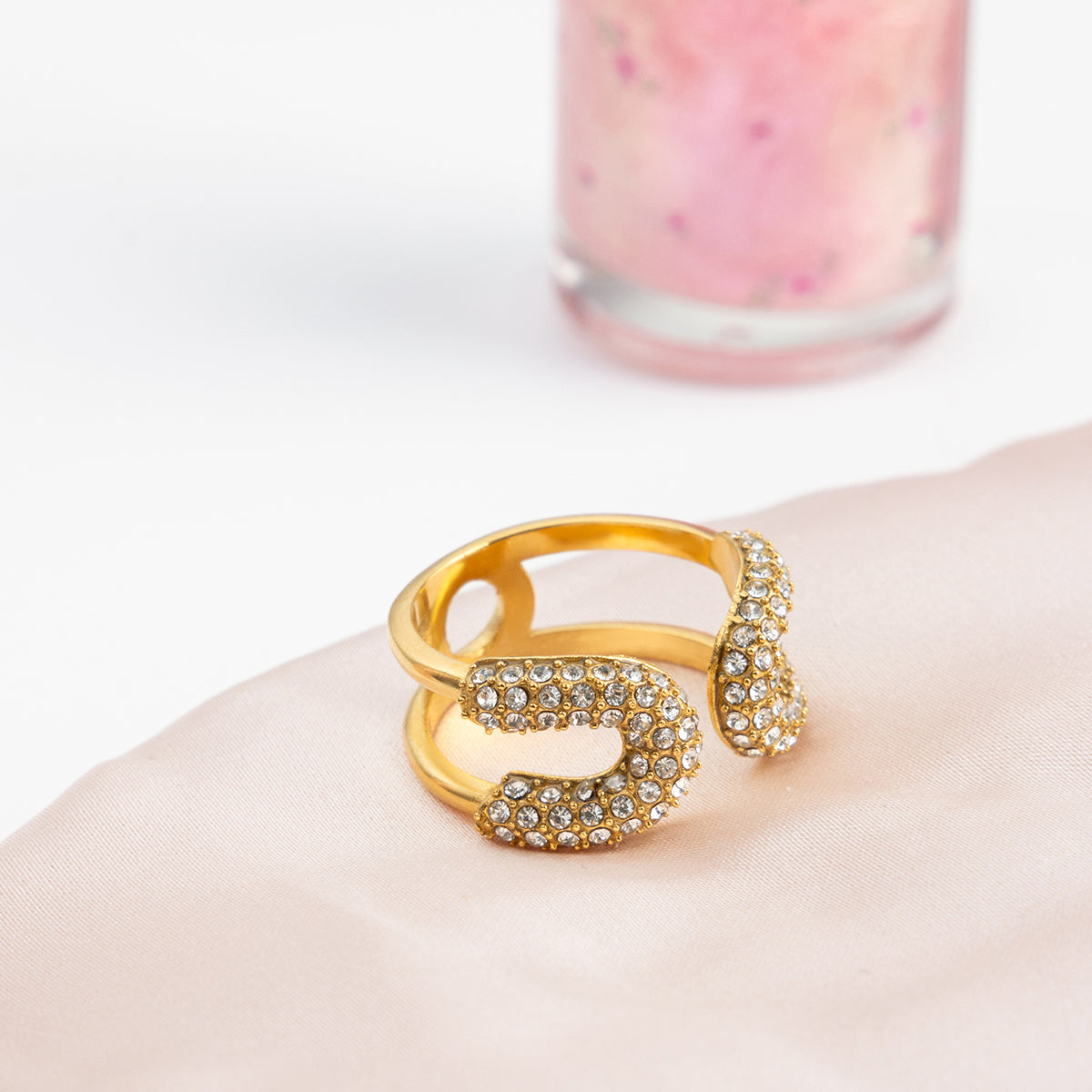 Gold ring with gemstones on a white surface with a blurred pink object in the background