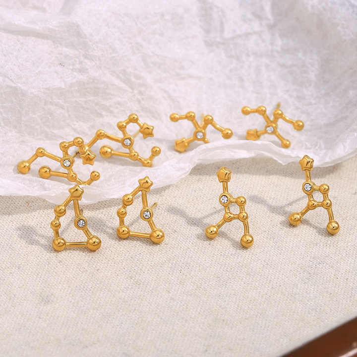 Gold constellation earrings on a textured surface