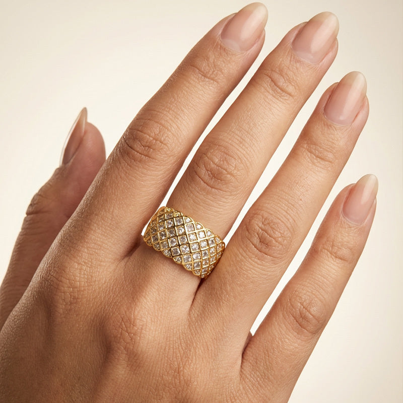 Gold ring with diamond pattern on a hand against a beige background