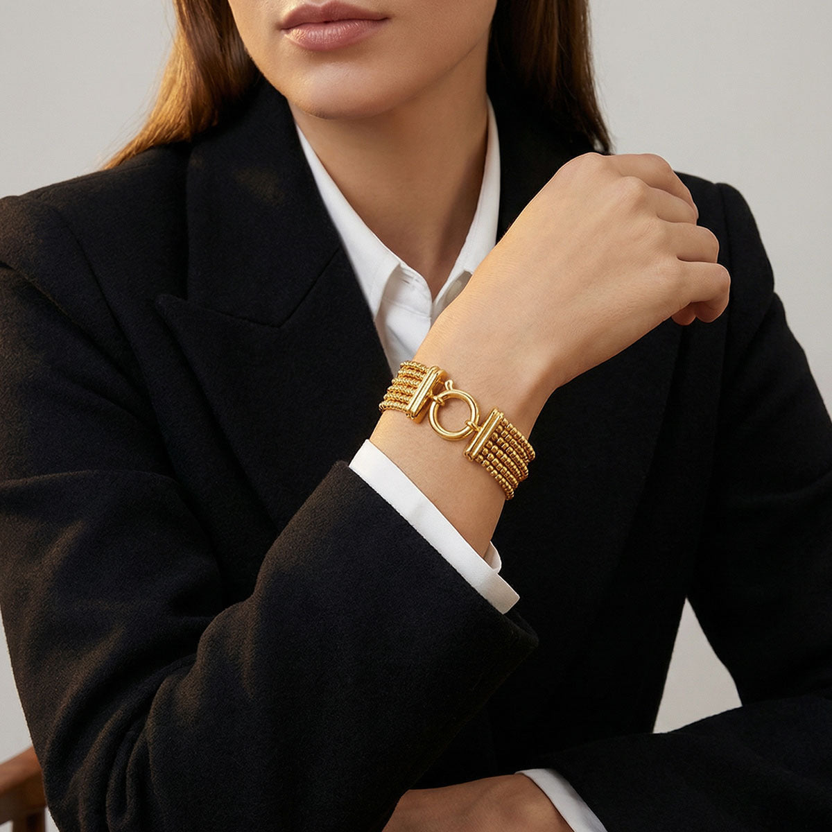 Woman wearing a gold bracelet on her wrist, dressed in a black blazer and white shirt.