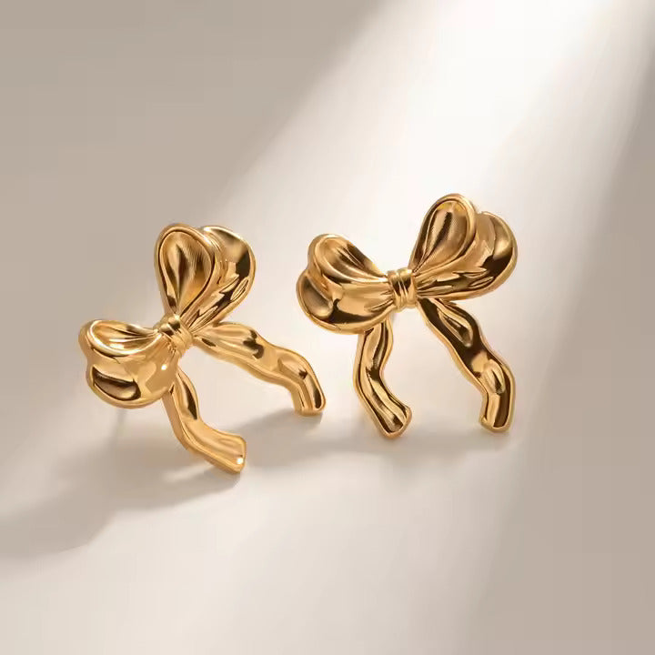 Gold bow-shaped earrings on a beige background