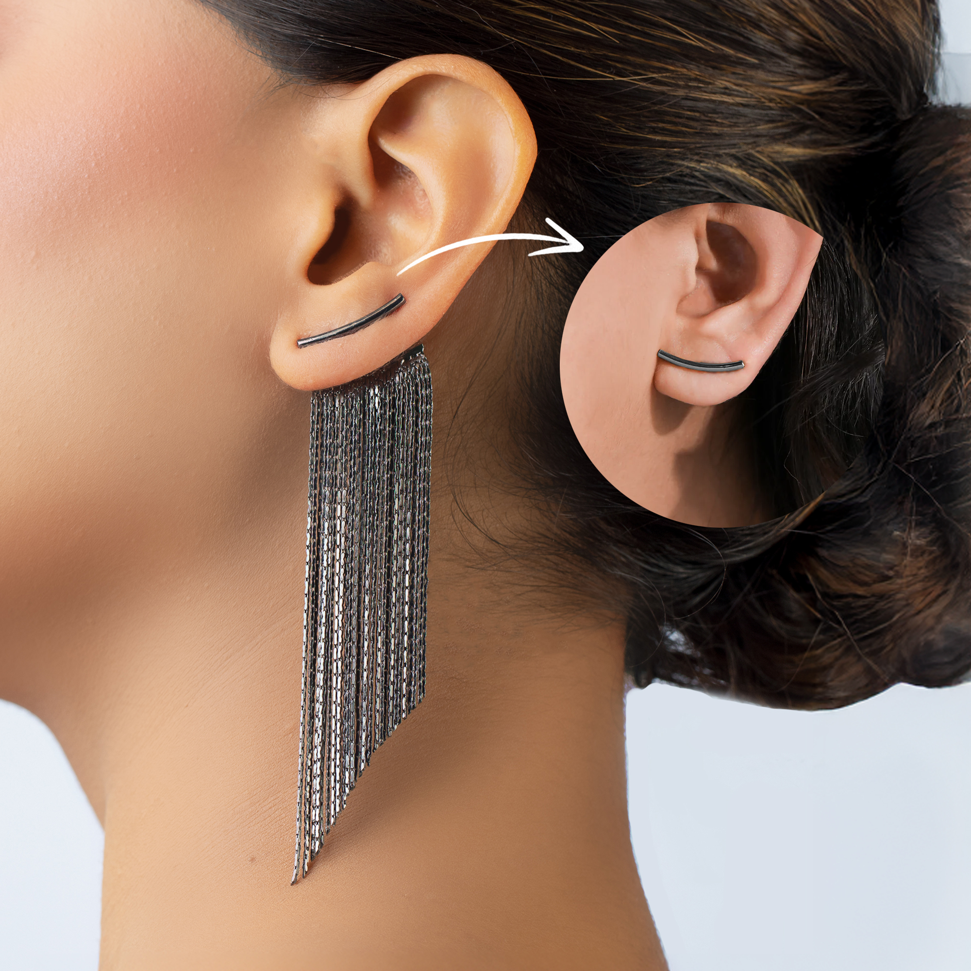 Close-up of a person wearing a long chain earring and a small hoop earring on a plain background