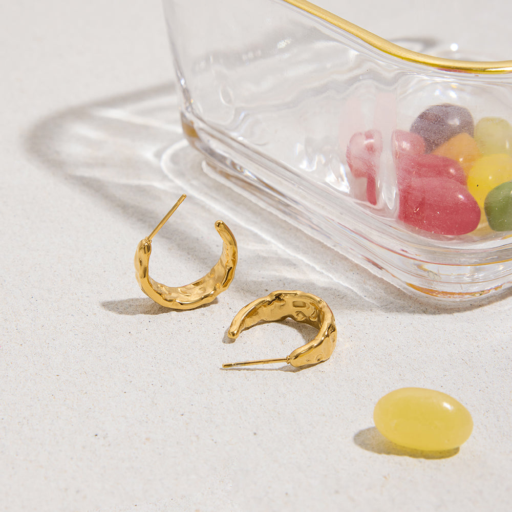 Gold hoop earrings for women on a white surface with colorful jelly beans in the background.