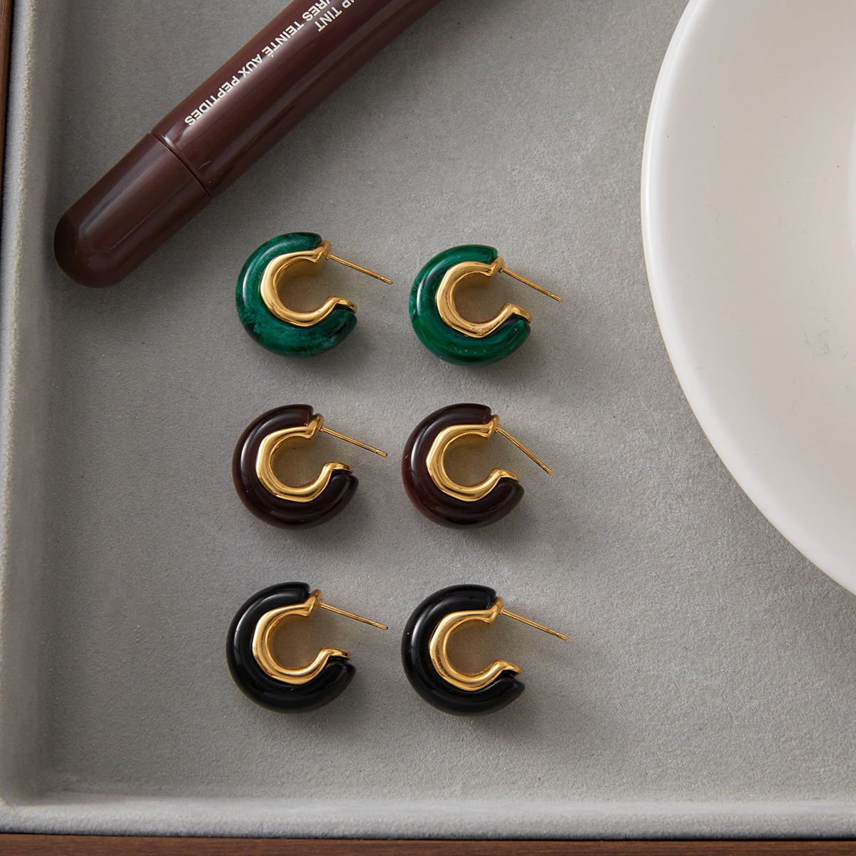 Set of hoop earrings in green, gold, brown, and black on a gray surface.