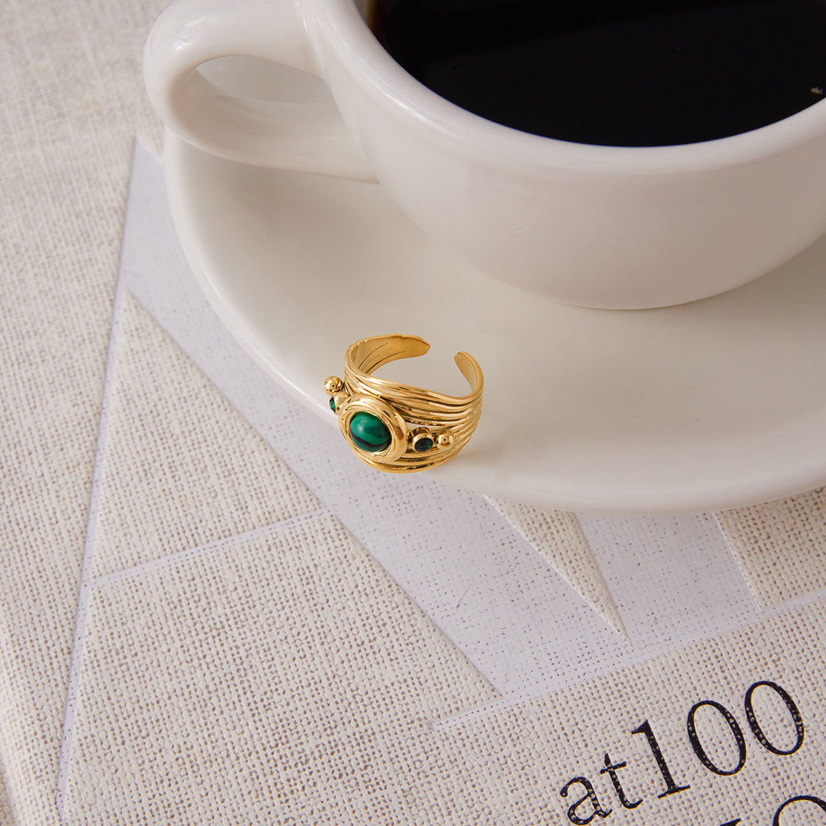 Gold ring with green gemstone on a white saucer next to a cup of coffee.
