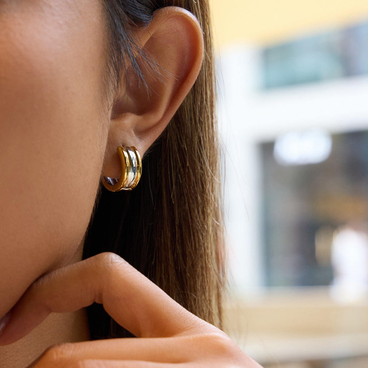 Close-up of a person wearing gold hoop earrings with a blurred background