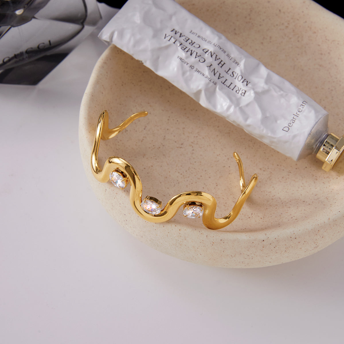Gold bracelet with crystals on a beige dish with a white background