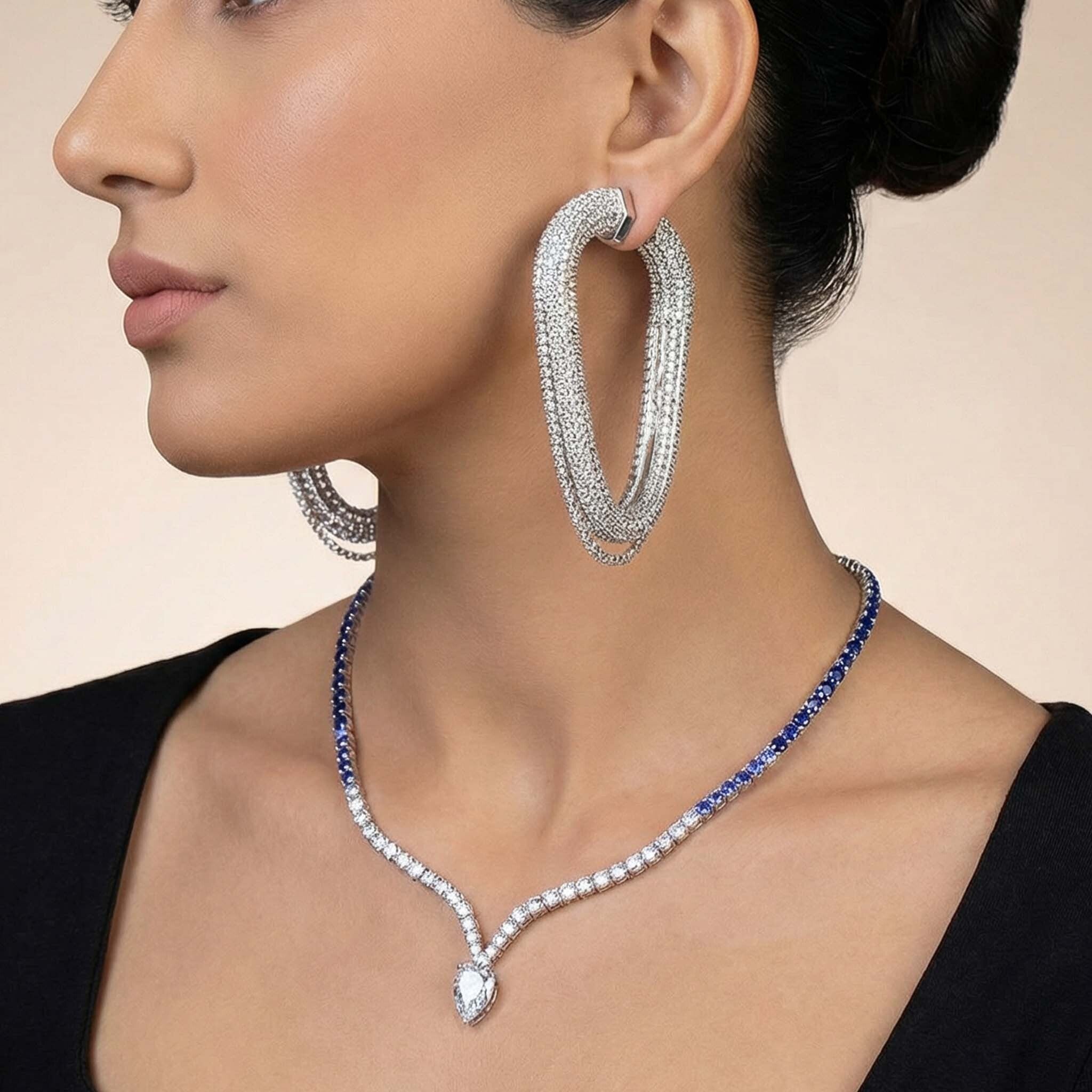 Close-up of a woman wearing silver hoop earrings and a blue and silver necklace against a beige background
