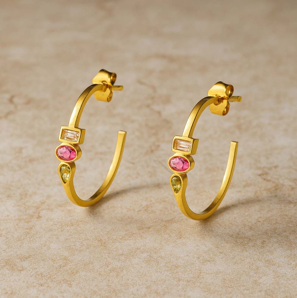 Gold hoop earrings with gemstones on a beige background