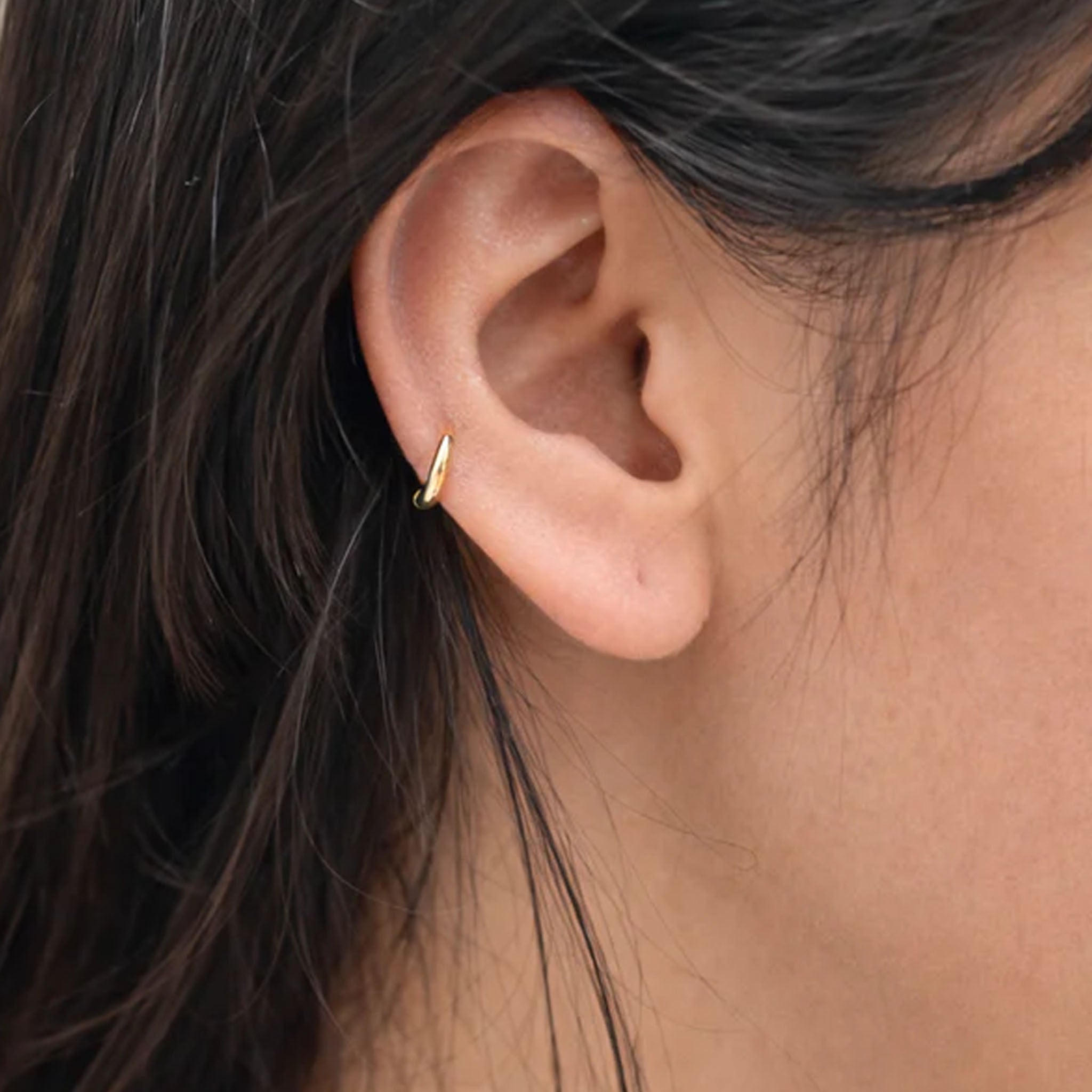 Close-up of an ear wearing a gold earring with dark hair and skin in the background