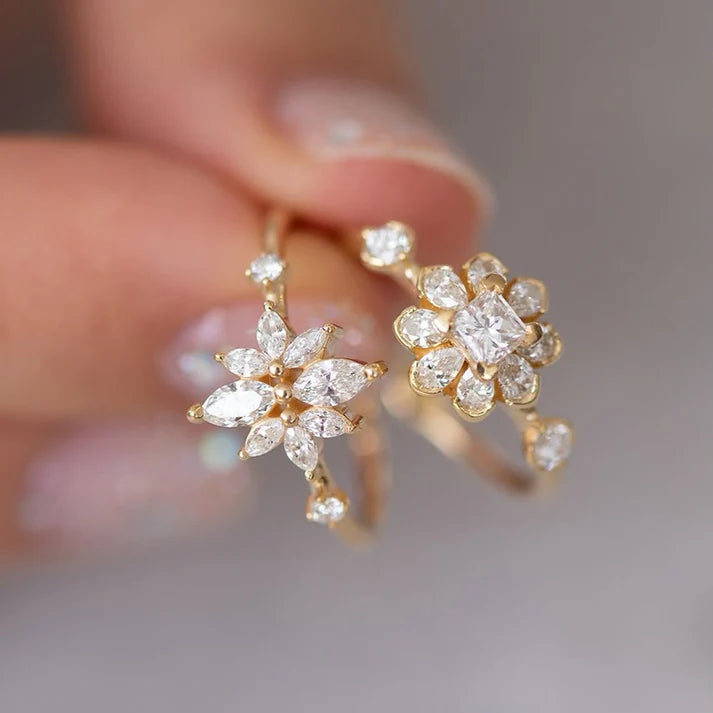 Gold earrings with clear gemstones held by a hand against a neutral background