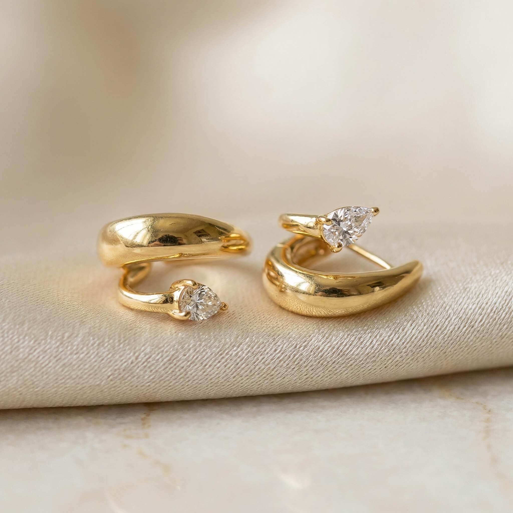 Two gold earrings  with diamond accents on a beige fabric background