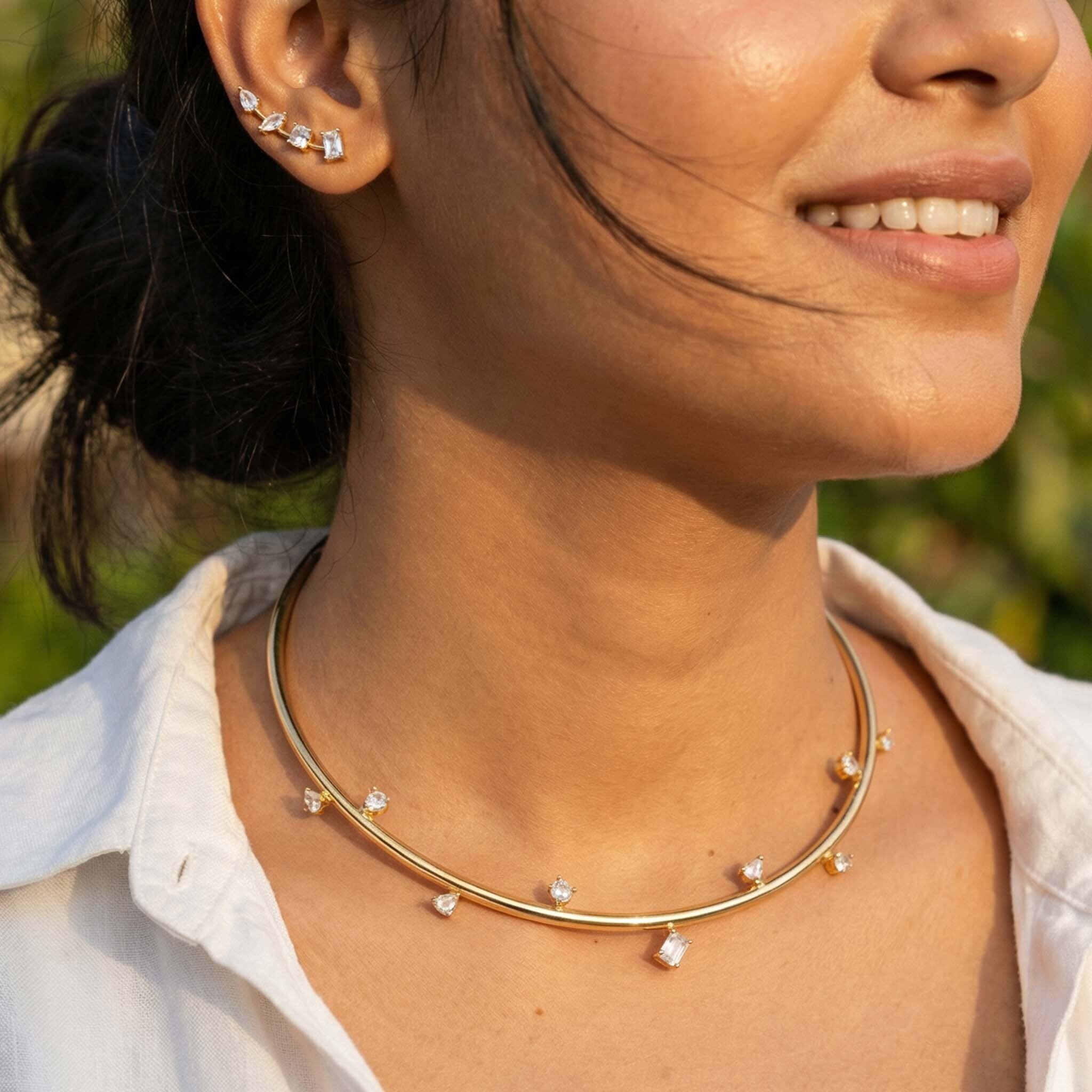 Close-up of a woman wearing a gold necklace with small stones, outdoors.