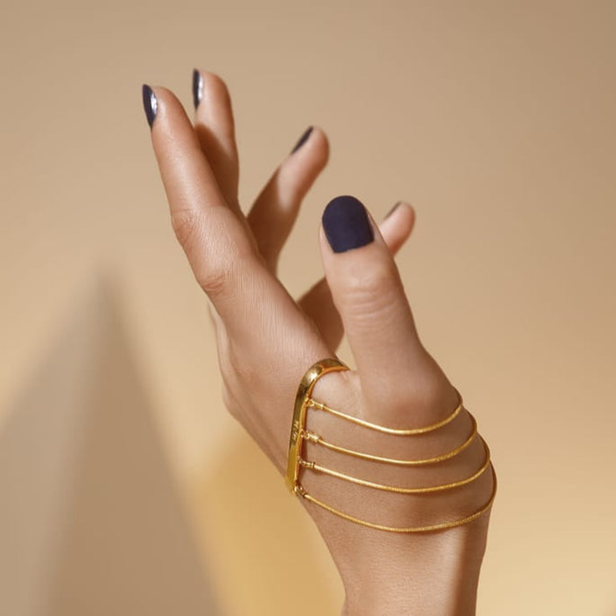 Hand wearing a gold ring with multiple bands on a beige background