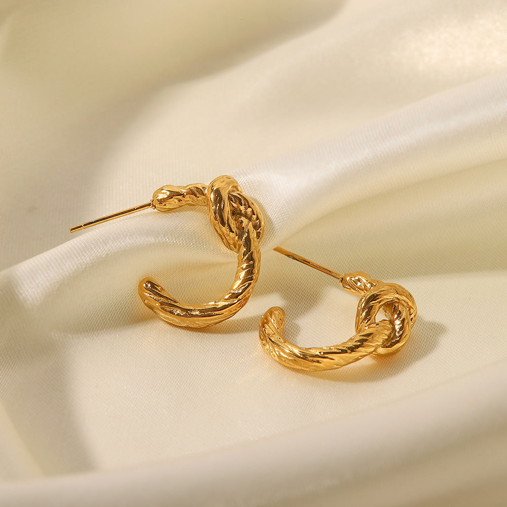 Gold twisted knot hoop earrings displayed on cream satin fabric