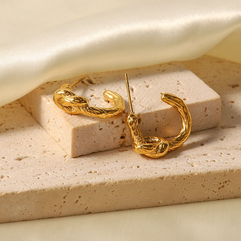 Textured gold knot hoop earrings displayed on beige stone blocks with satin fabric background