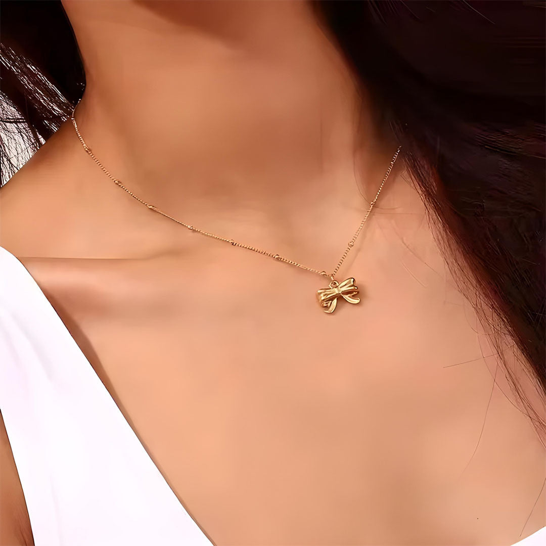 Gold necklace with a bow pendant on a person's neck