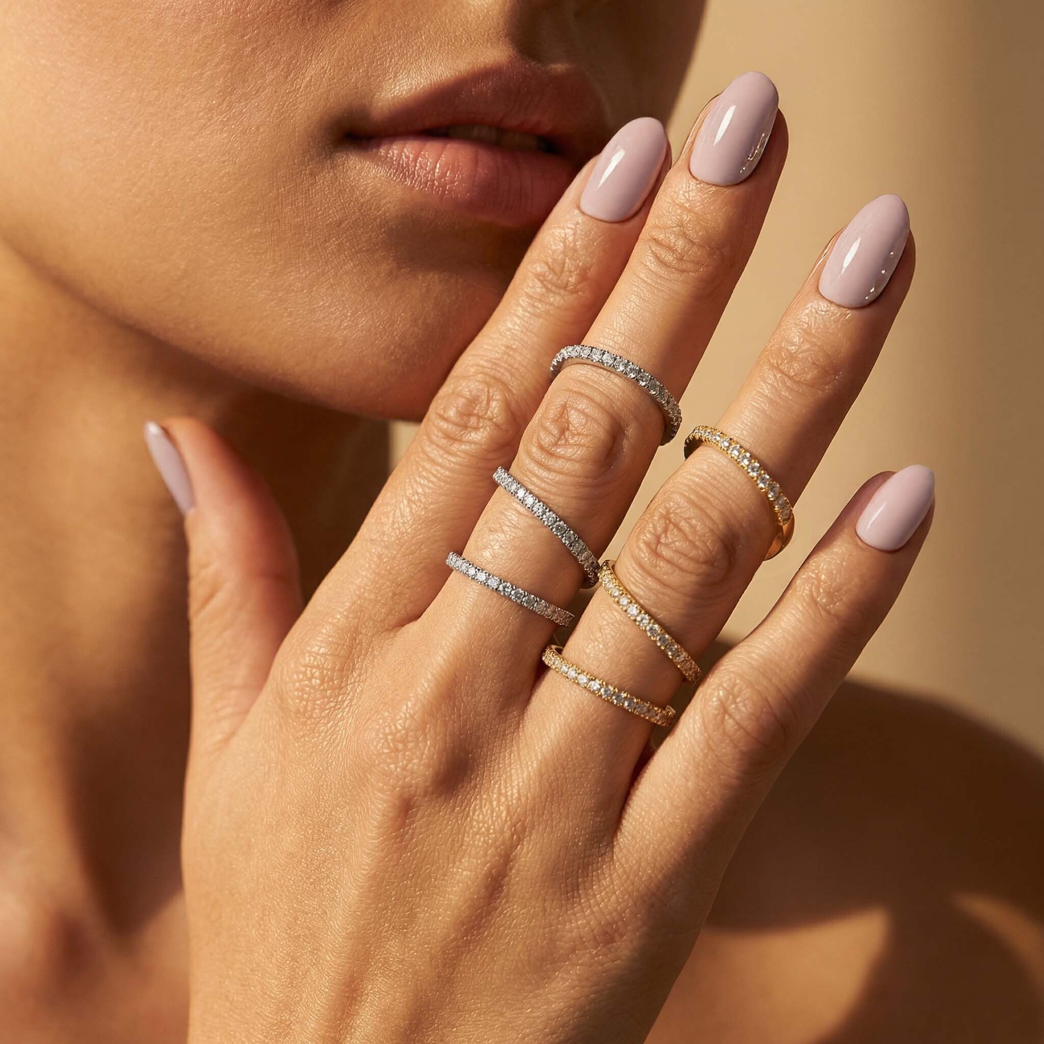 Close-up of a hand with multiple rings and light pink nail polish on a neutral background