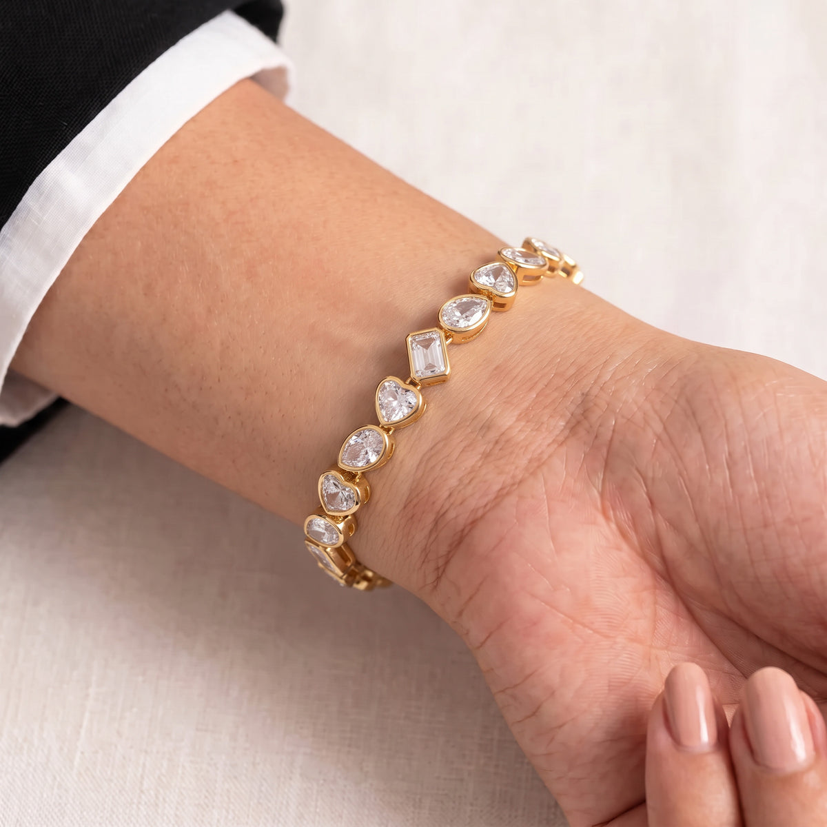 A gold bracelet with clear gemstones worn on a person's wrist, shown against a light neutral background.