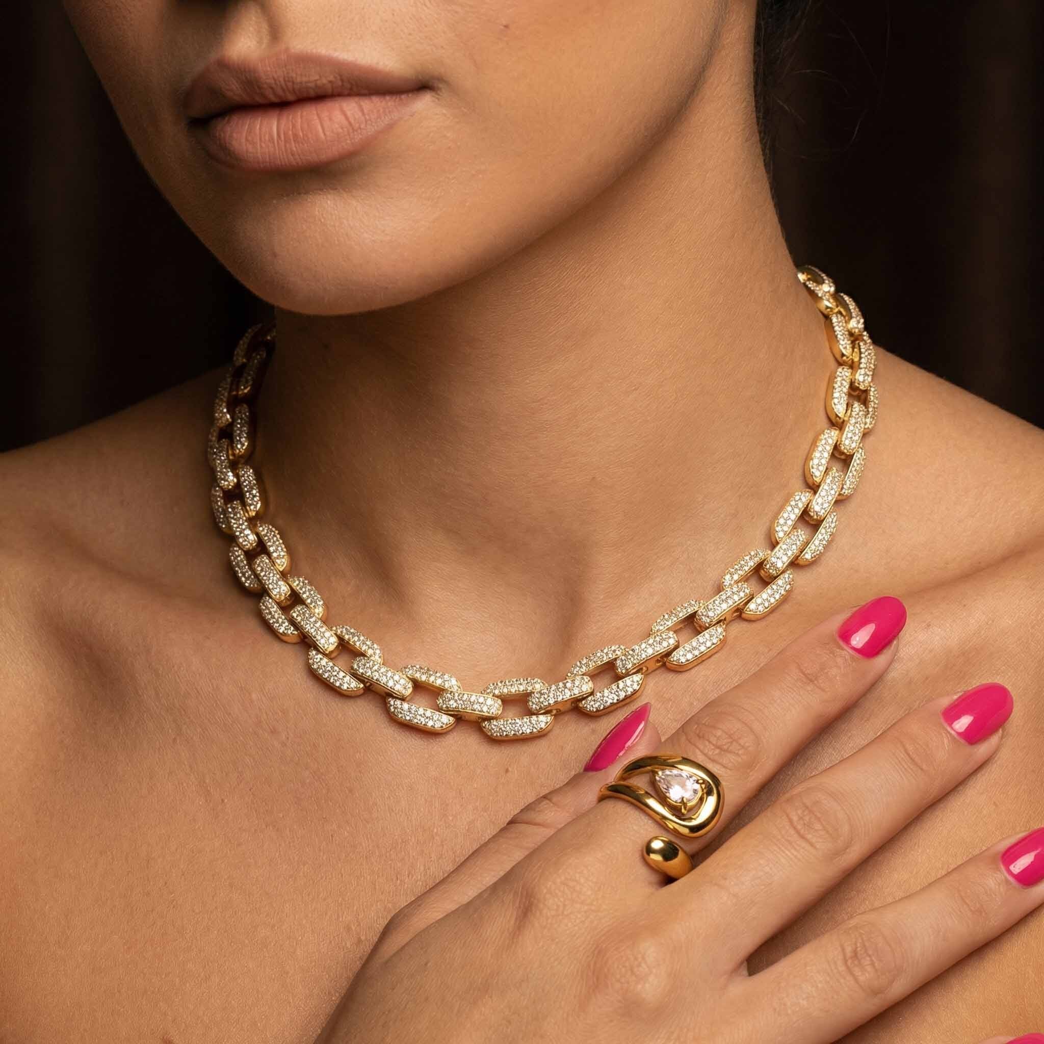 Gold chain necklace and ring on a model with pink nail polish