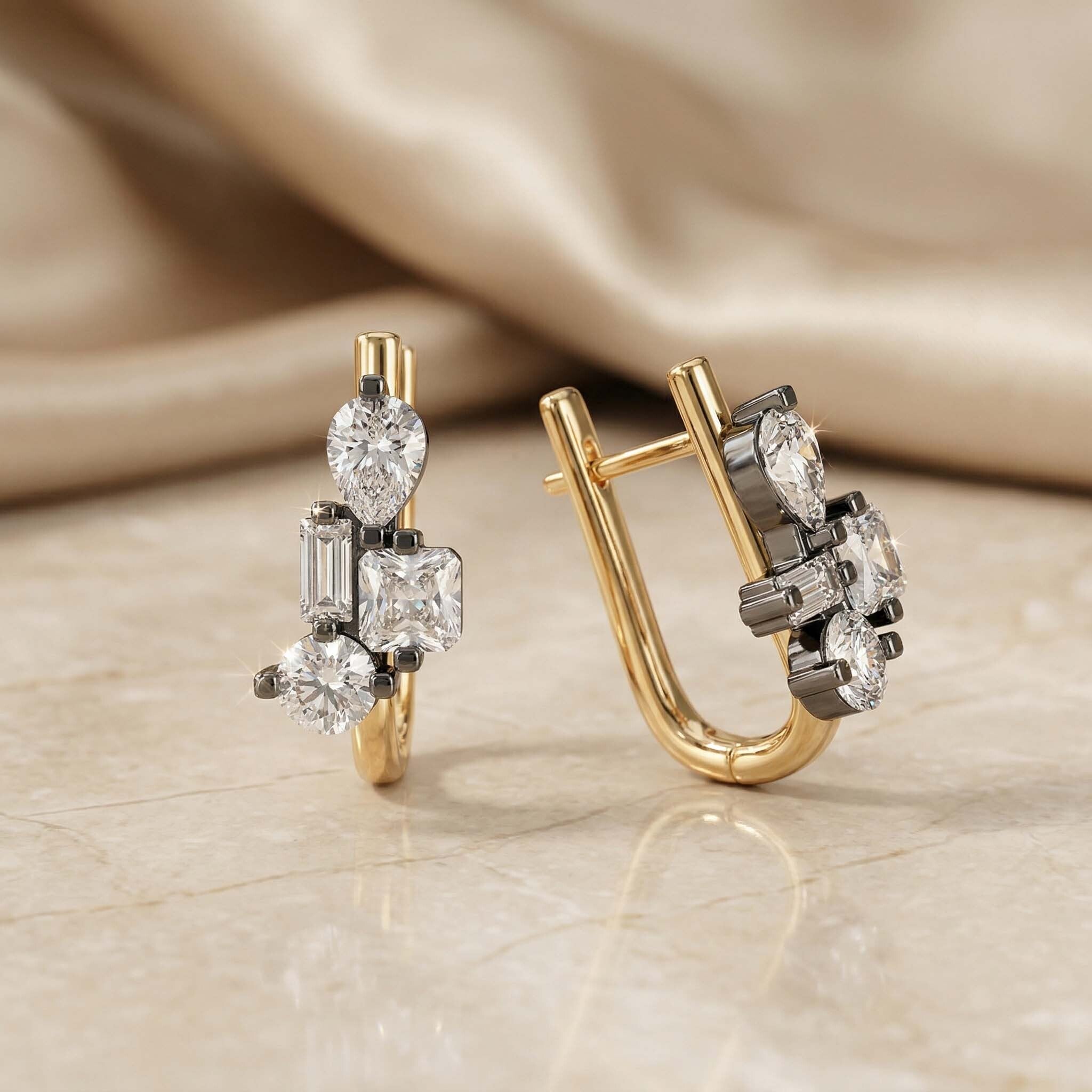 Gold and silver earrings with diamond accents on a beige fabric background