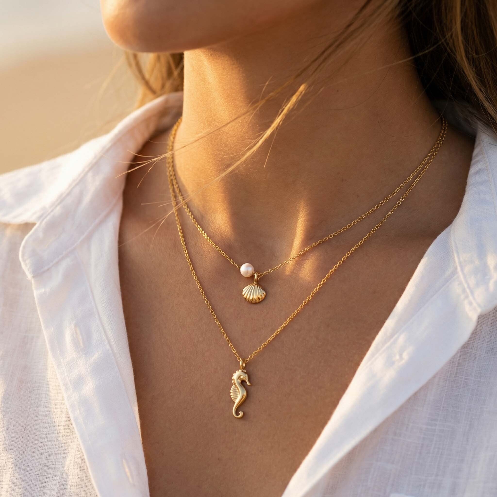Close-up of a person wearing a gold necklace with seahorse and shell pendants against a blurred background.