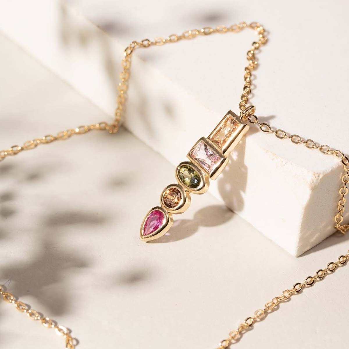 Gold necklace with multicolored gemstones on a soft white background