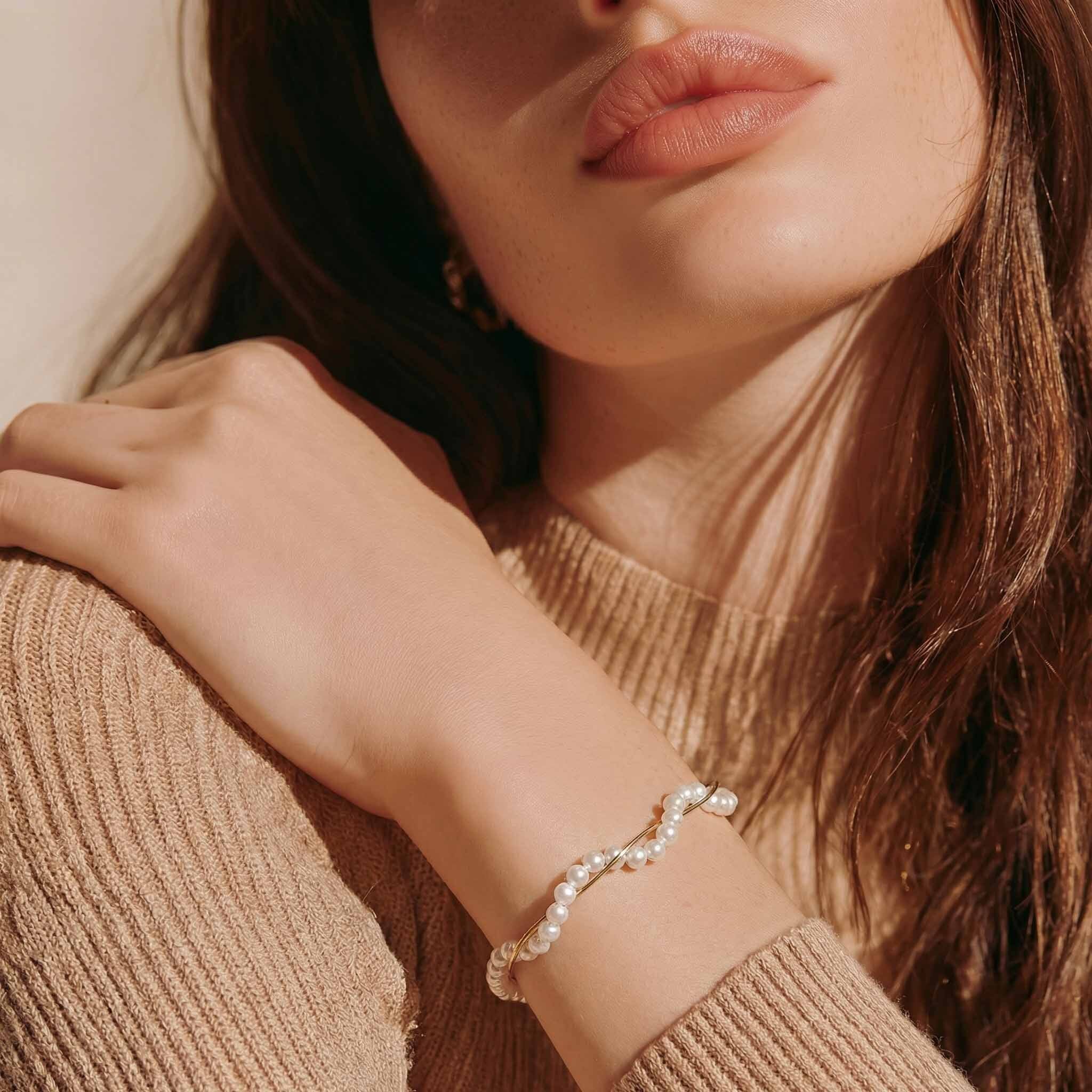 Close-up of a woman wearing a pearl bracelet on a beige sweater.