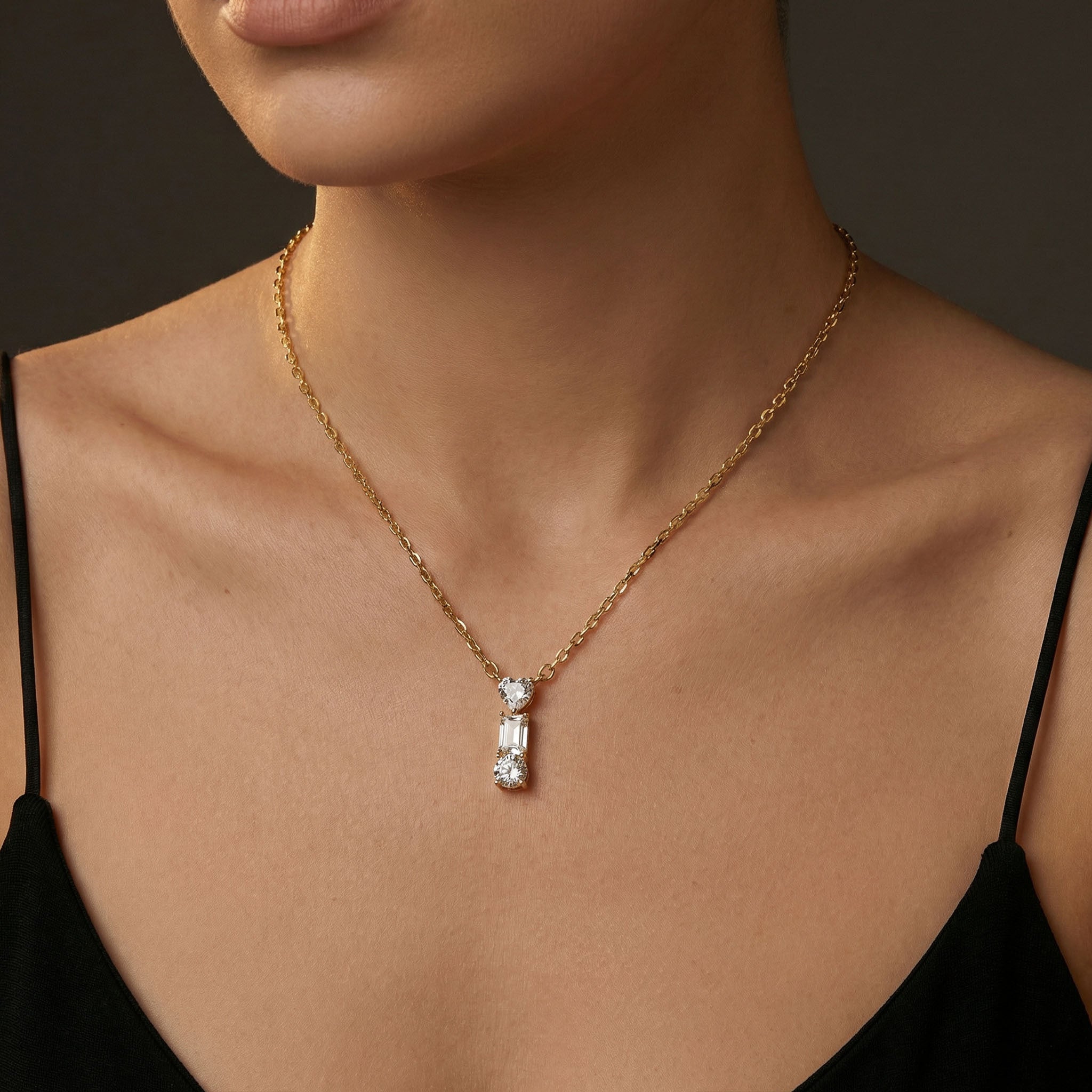 Gold necklace with a pendant on a person wearing a black top against a dark background