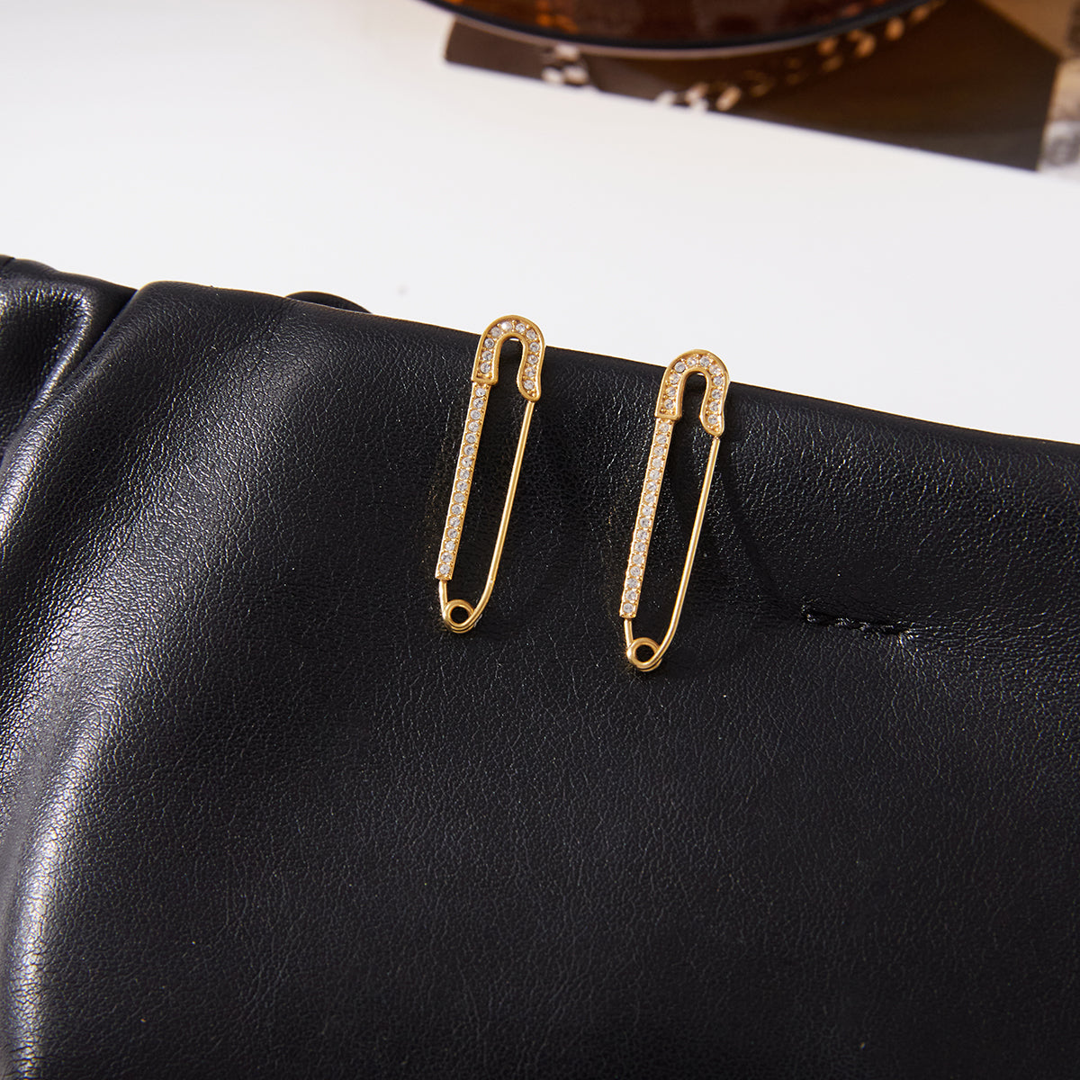 Gold safety pin earringson a black leather surface